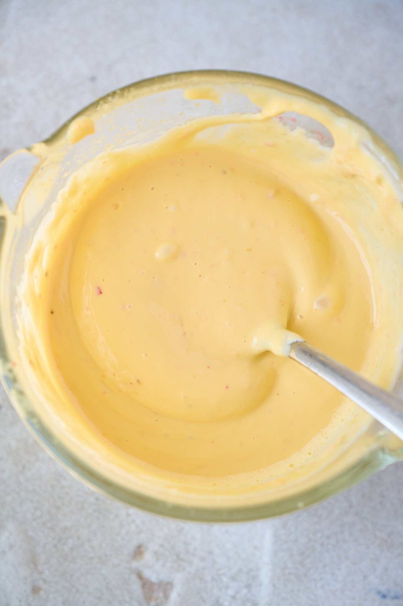 Olive oil mayonnaise is in a glass jar with a spoon in it. 