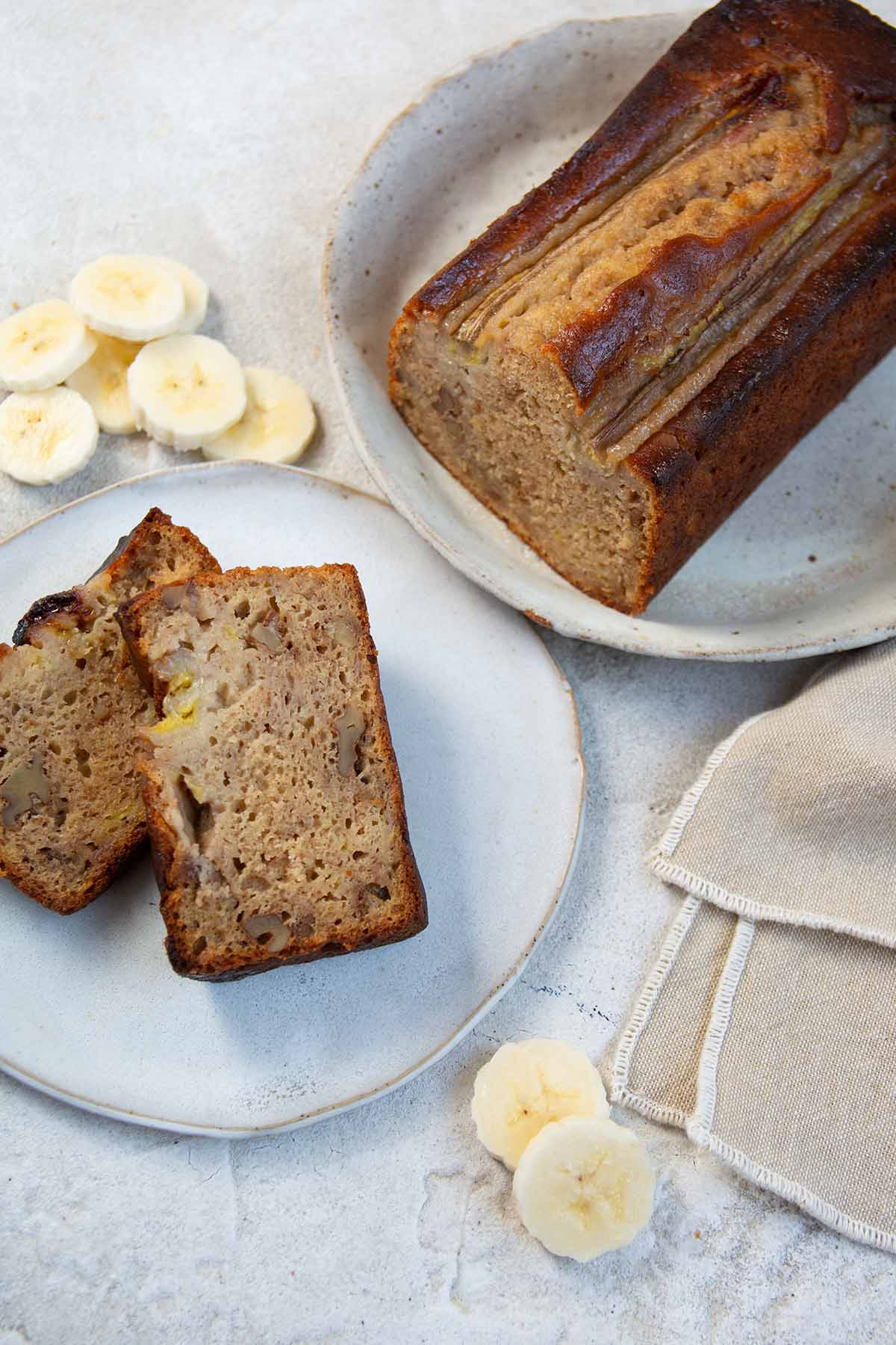 two slices of banana bread on a white plate with the loaf.