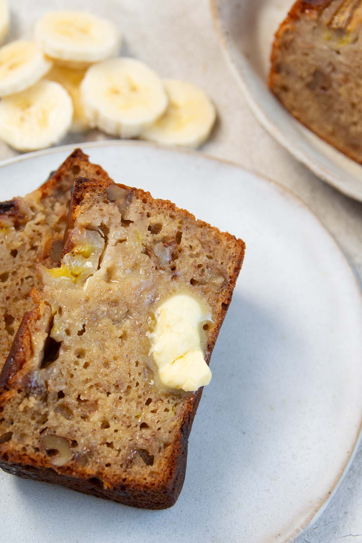 buttered slice of banana bread on a white plate.