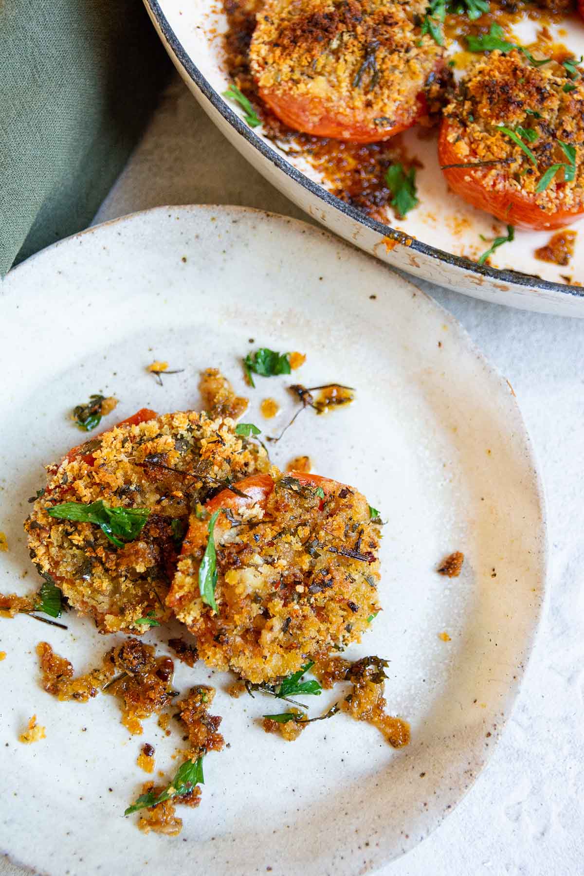 two stuffed tomatoes on a white plate with a green napkin.