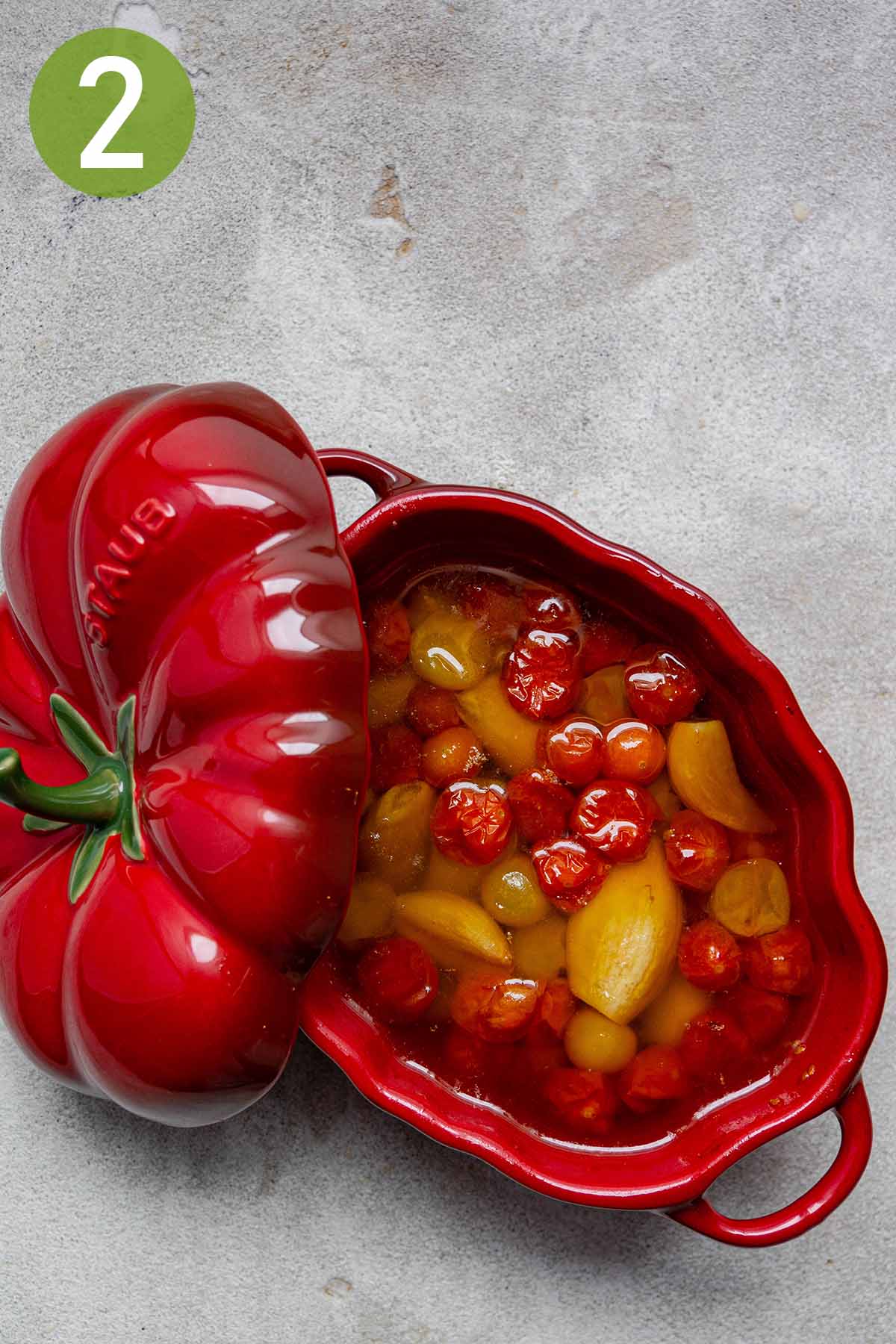 baked tomato and garlic confit in a red pot.