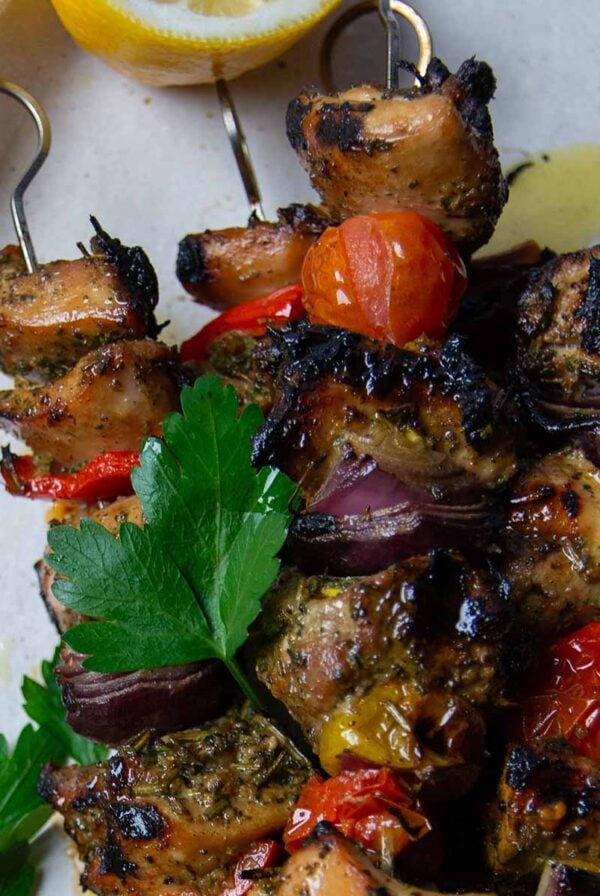 white plate of chicken skewers with parsley and half of a lemon.
