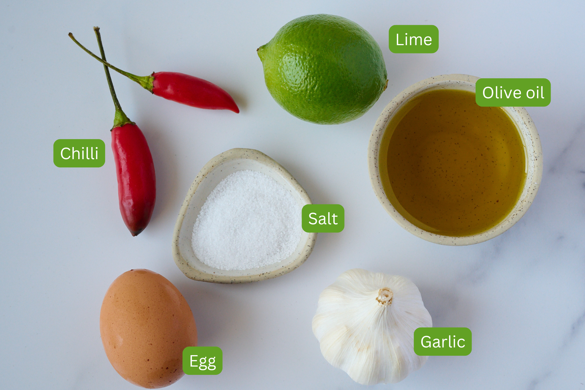 Ingredients are laid out on a marble background. Ingredients include chilli, salt, lime, olive oil, garlic and egg. 