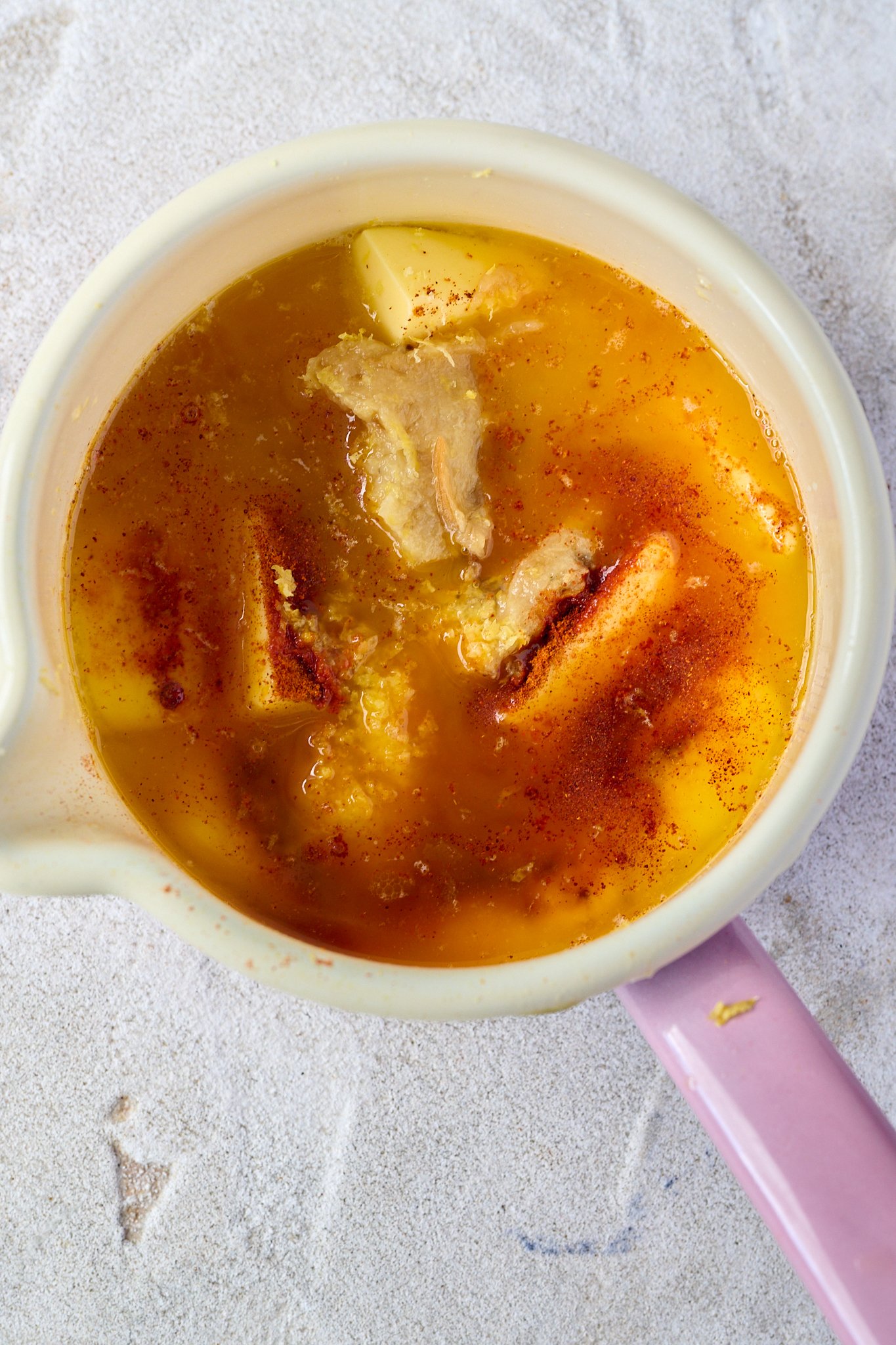 Butter and spices sit in a white bowl with a pink handle. 