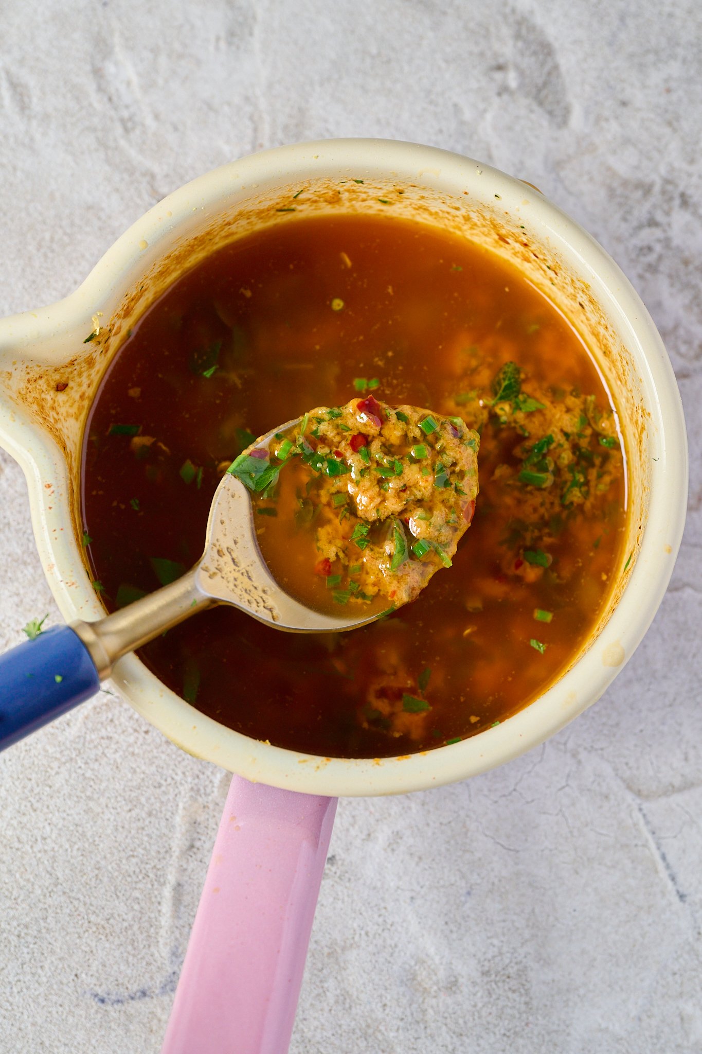 Butter, herbs and spices sit in a white bowl with a pink handle. 