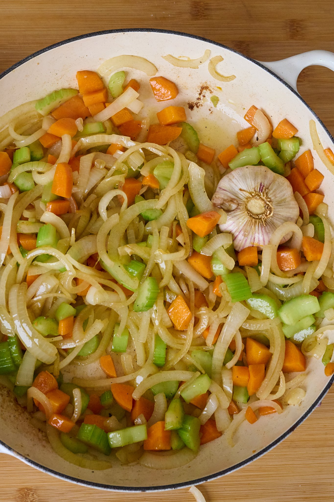 Carrots, onion, celery and garlic have been fried in a large white pan with a blue rim. 