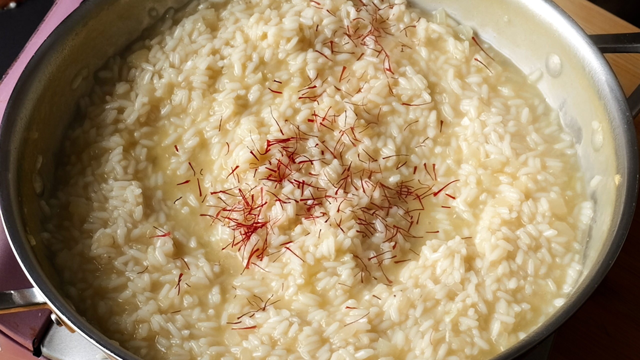 Image of stainless steel pan with plump rice and saffron threads on top. 