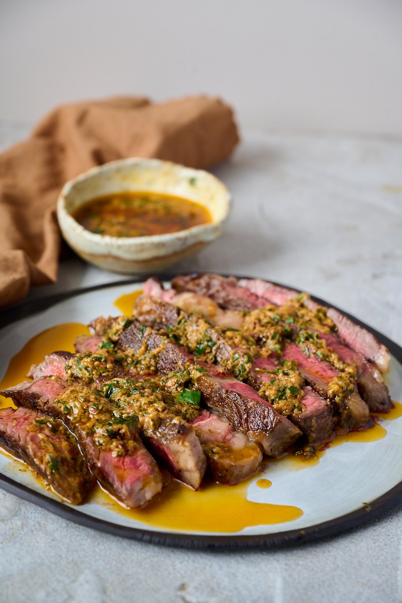 Cowboy butter has been drizzled onto sliced up steak that is sitting on a white plate with a black rim. 