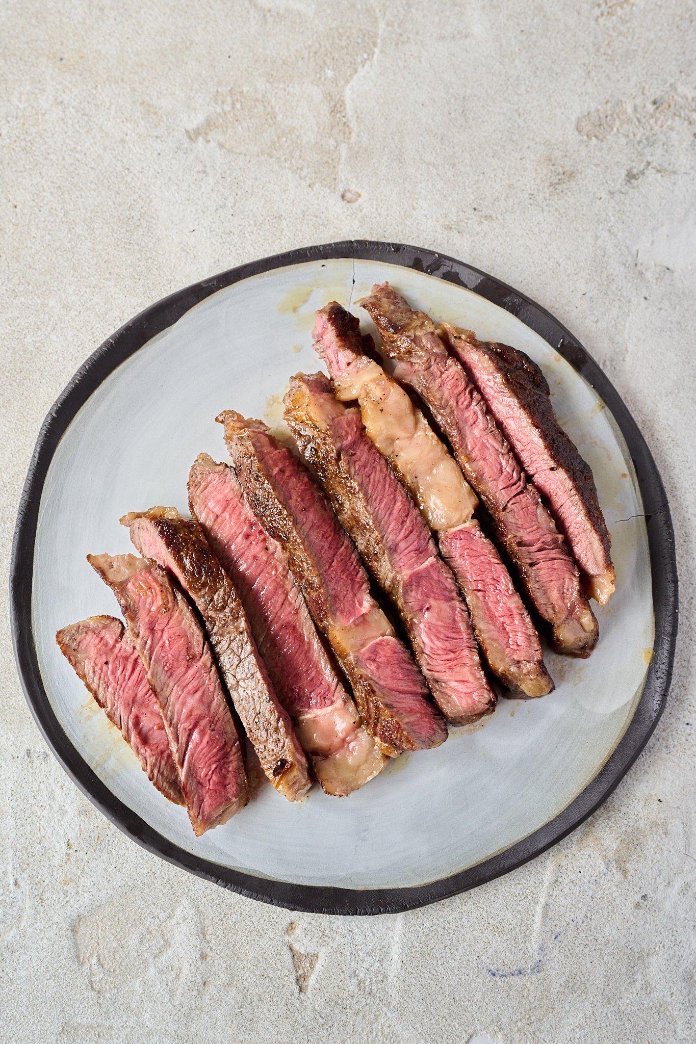 Cooked steak has been sliced and is pink inside. Sits on white plate with black rim. 
