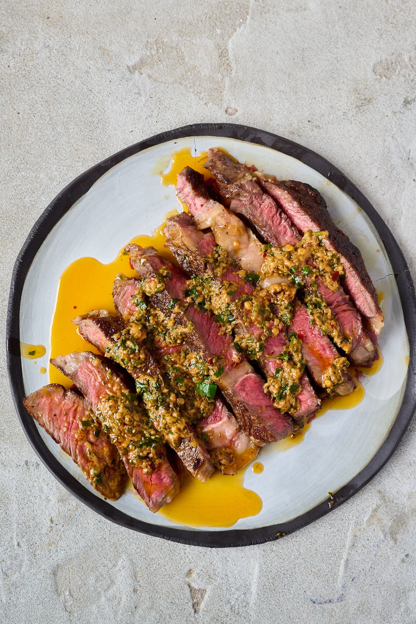 Cowboy butter has been drizzled onto sliced up steak that is sitting on a white plate with a black rim. 