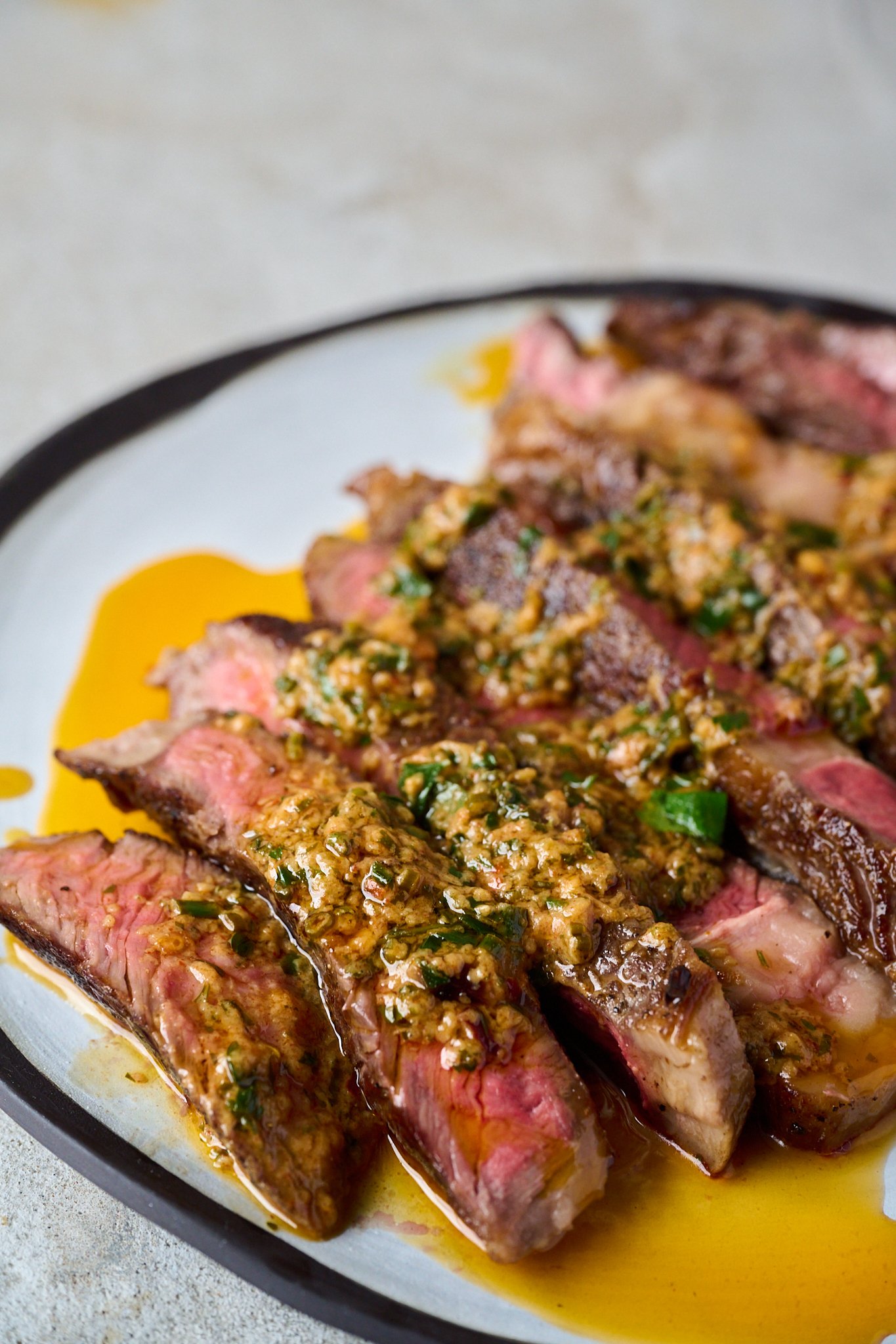 Cowboy butter has been drizzled onto sliced up steak that is sitting on a white plate with a black rim.