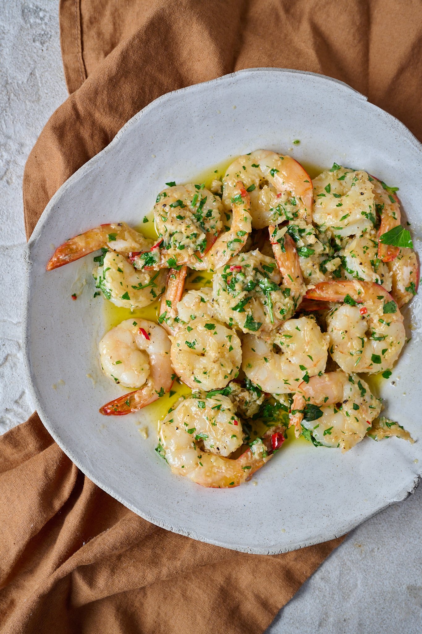 Garlic butter prawns / shrimp are in large white bowl and have fresh parsley sprinkled over top.