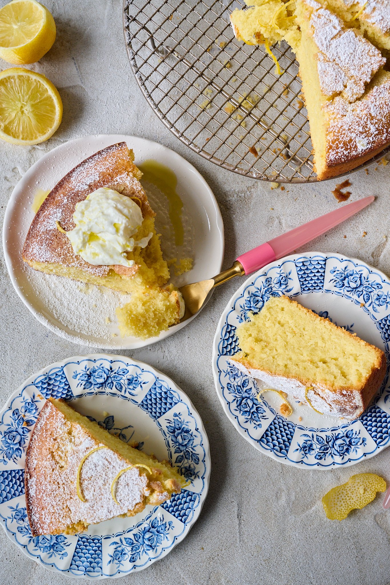Three slices of lemon olive oil cake are sitting on three different plats. One plate is white and has a pink fork on it that has taken a slice from the cake. The other two are blue floral plates. 