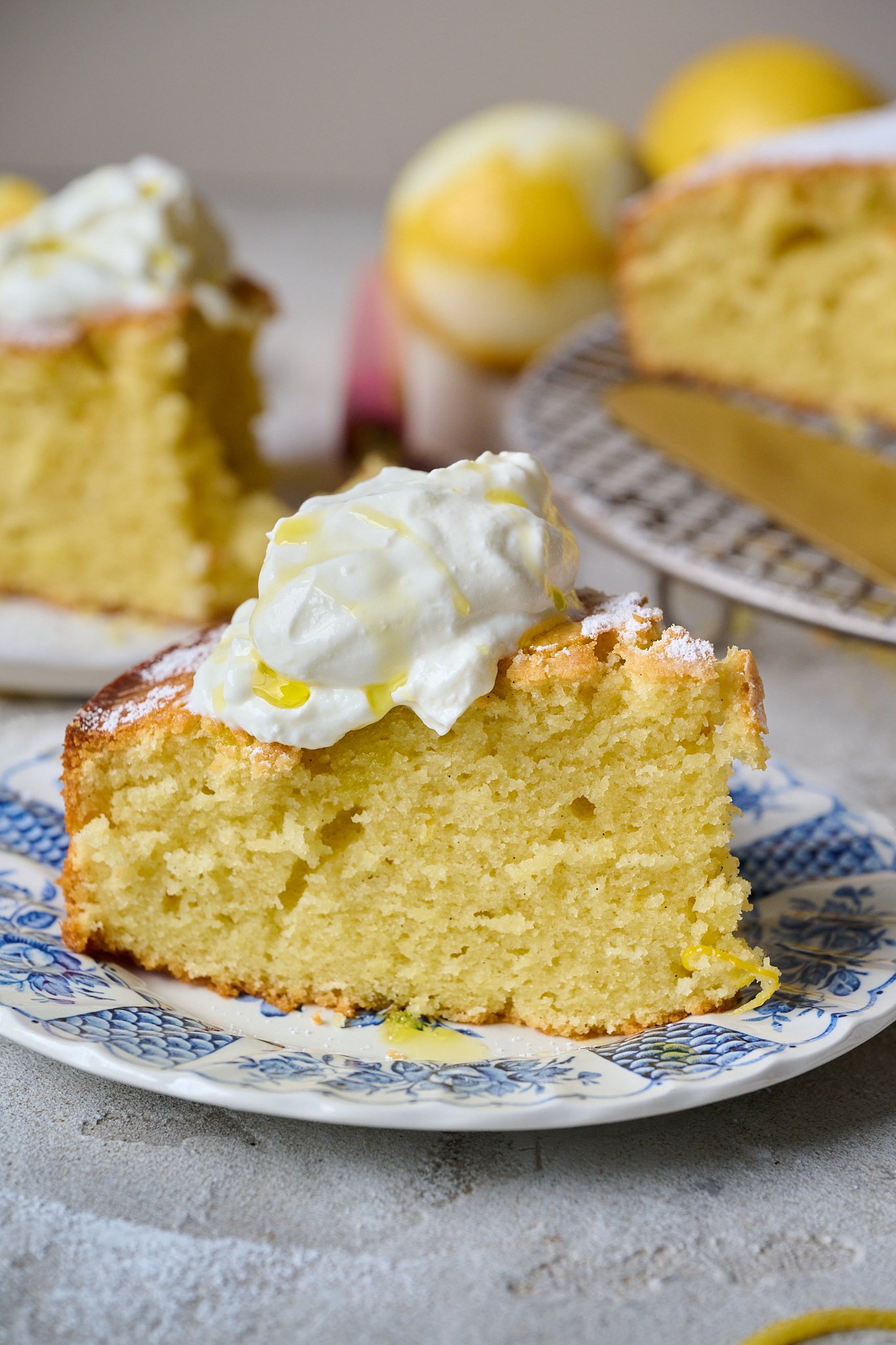 Slice of lemon olive oil cake sits on blue plate with dollop of greek yoghurt on top and drizzle of olive oil.