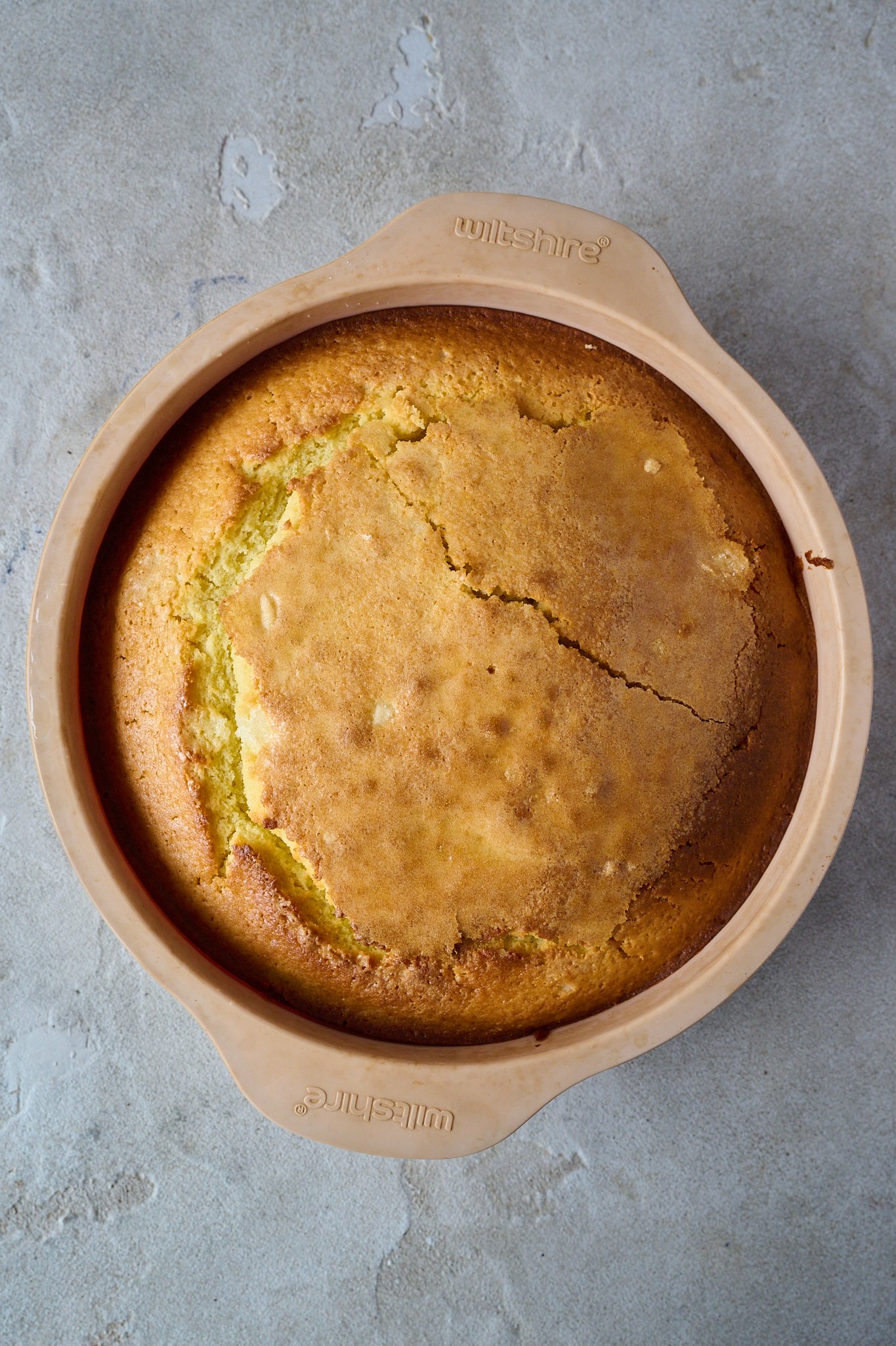Lemon olive oil cake is baked and sits in pink silicone tin. 