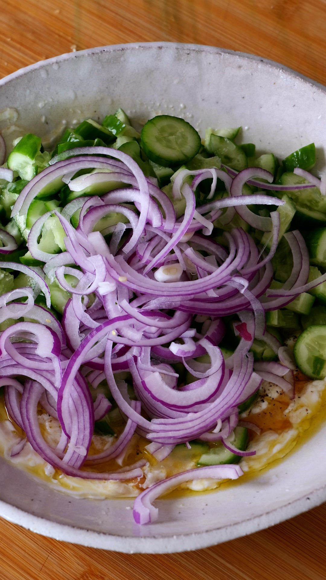 Cucumbers and red onion have been added to bowl with dressing. 