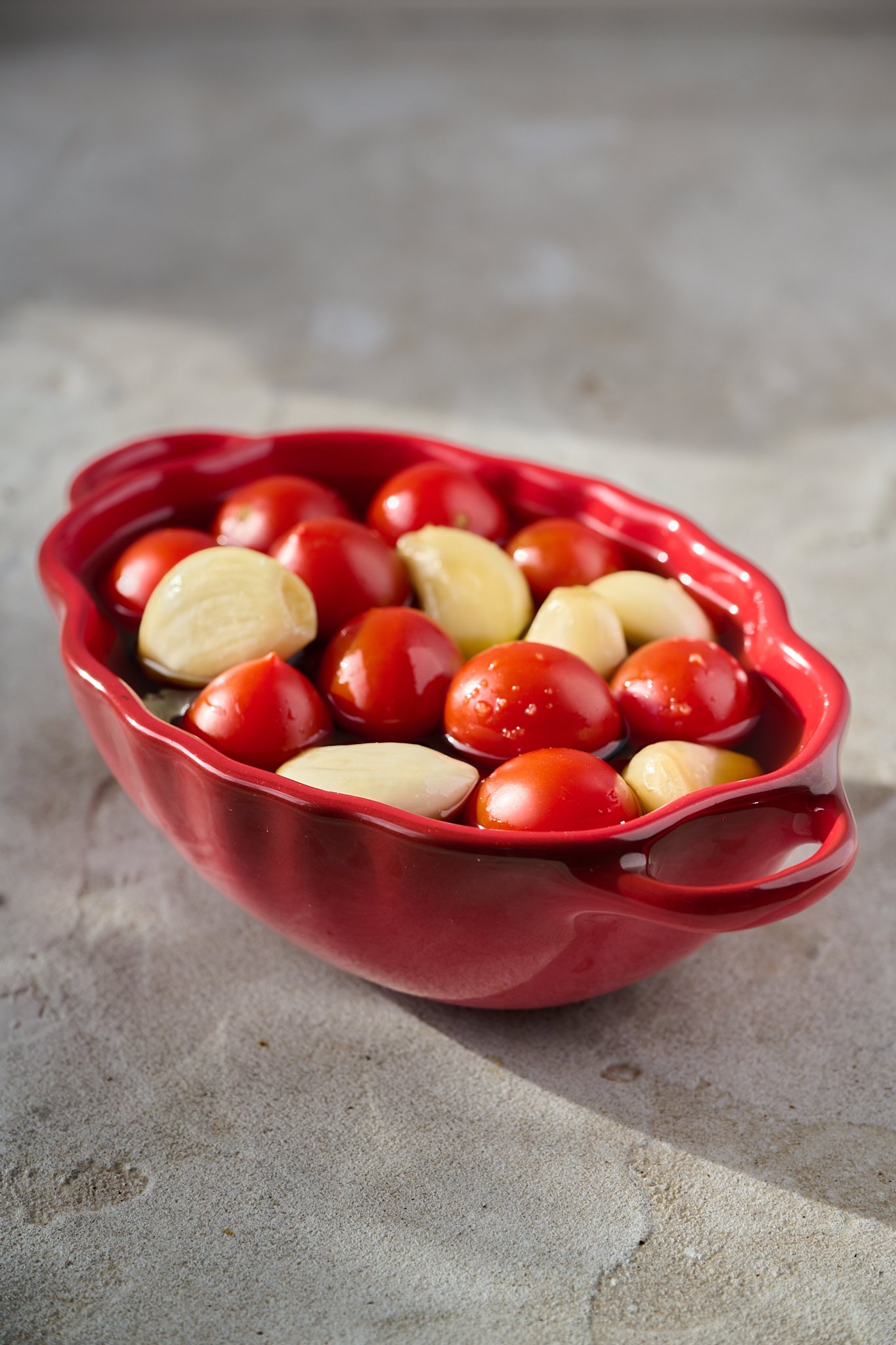 Tomatoes and garlic cloves sit in a red pot. 