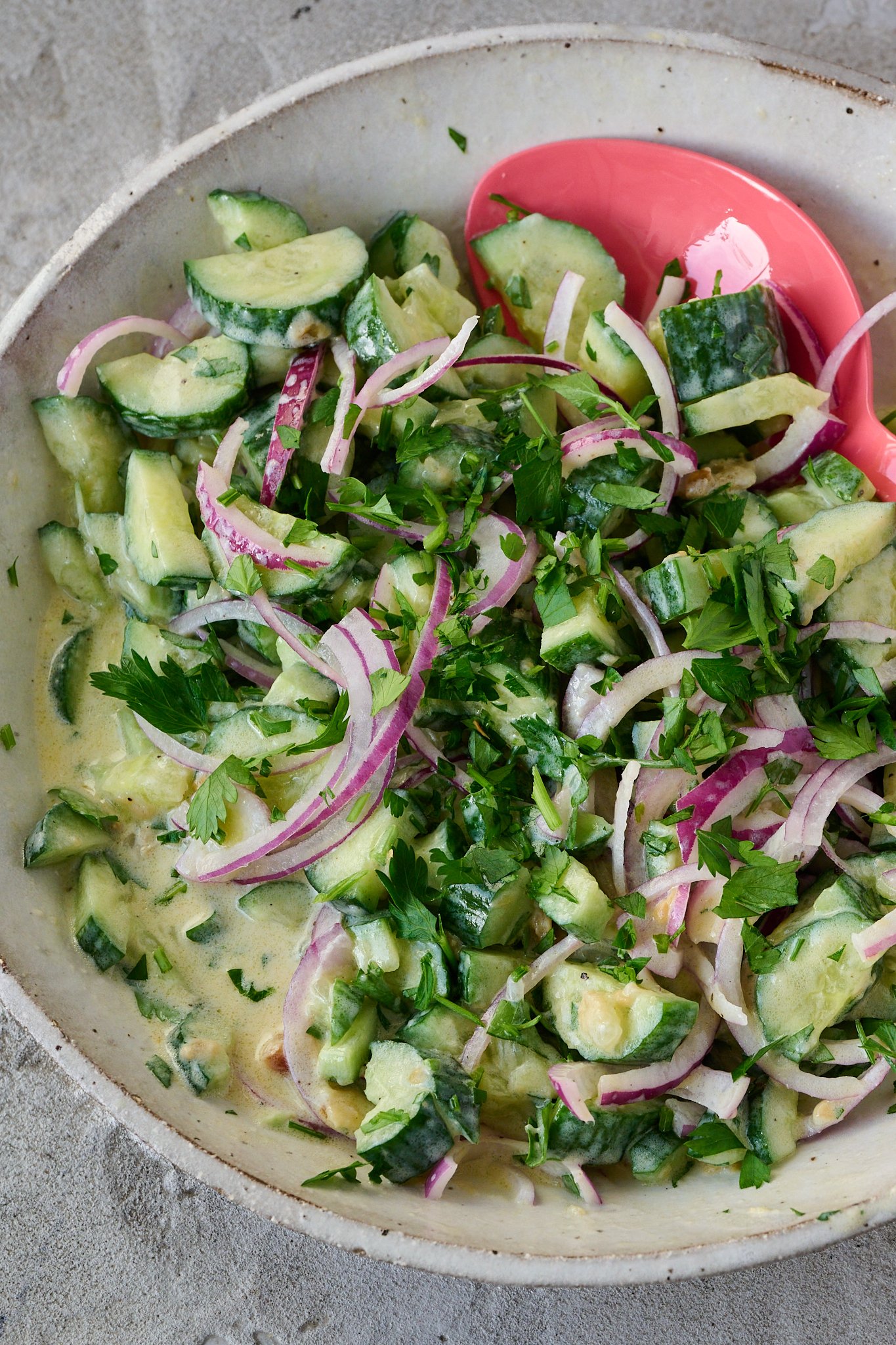cucumber salad with Greek yogurt sits in large white bowl with pink spoon poking out the side.