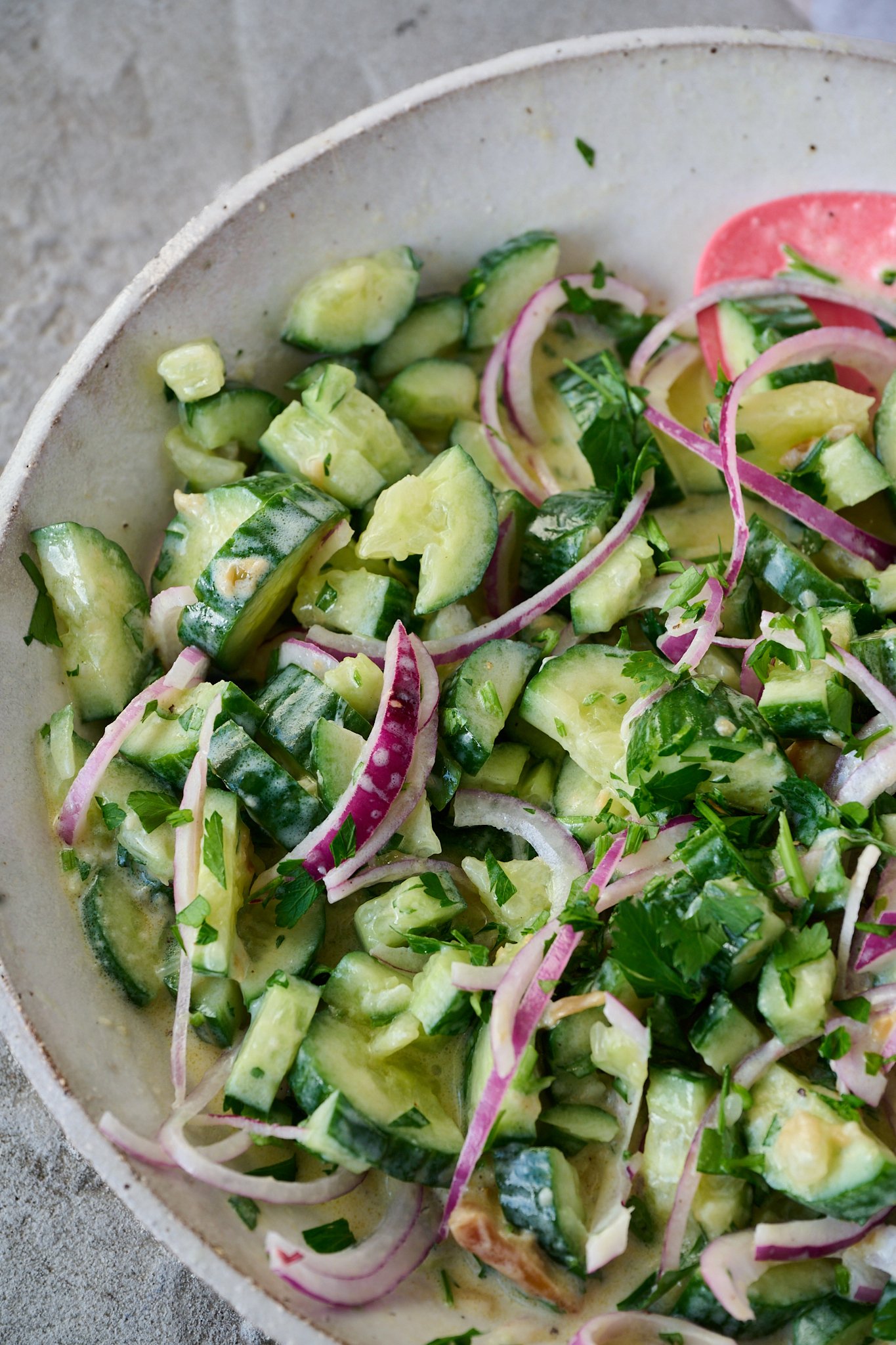 cucumber salad with Greek yogurt sits in large white bowl with pink spoon poking out the side. 