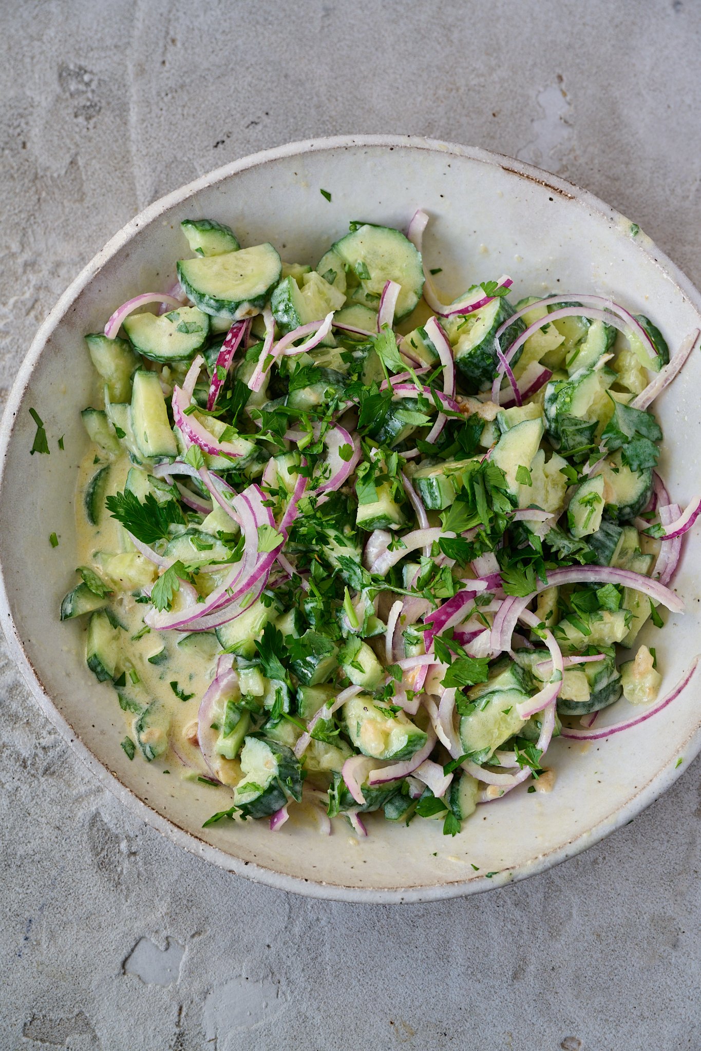 cucumber salad with Greek yogurt sits in large white bowl. 