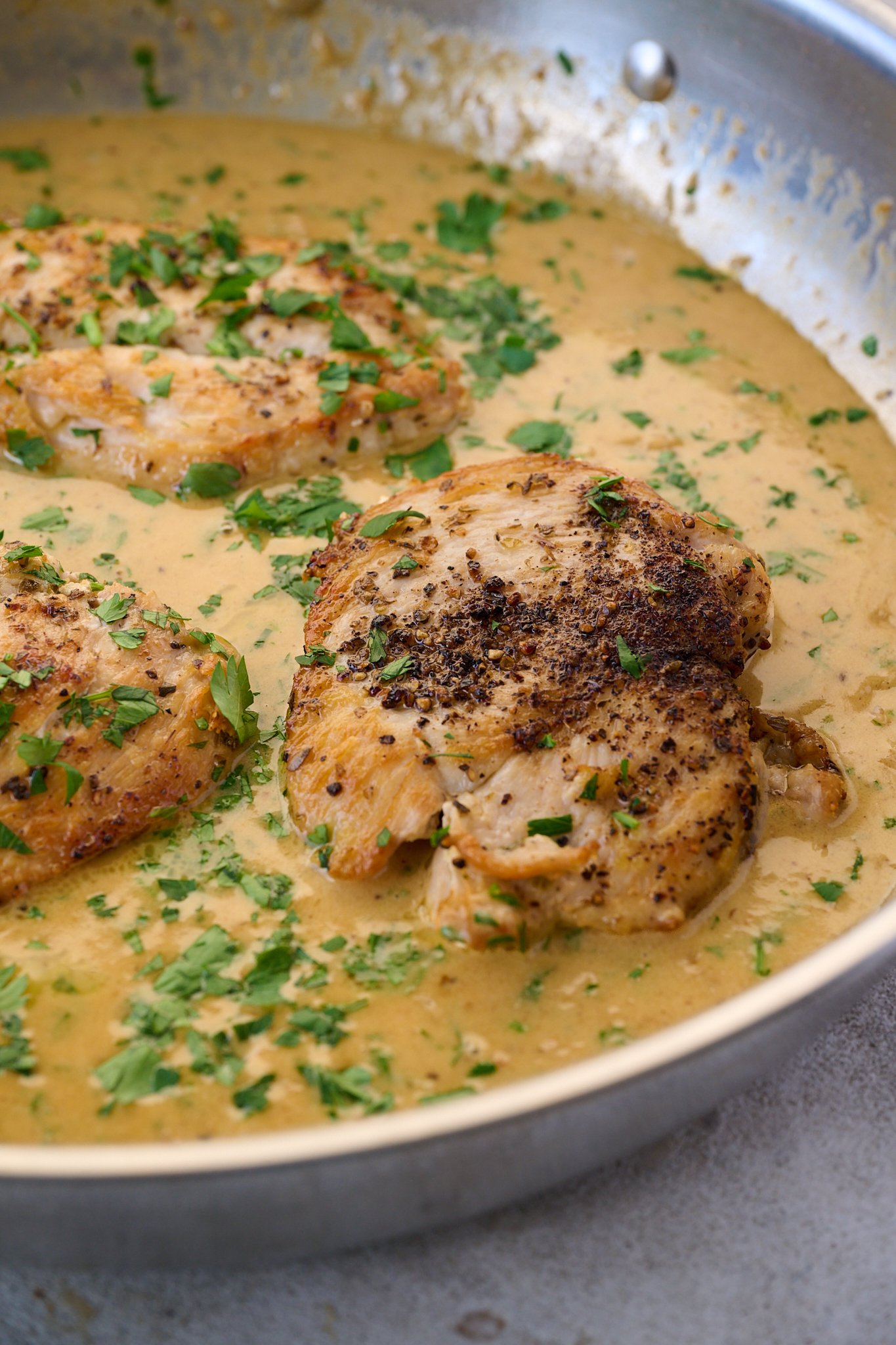 Creamy Garlic Parmesan Chicken sits in stainless steel pan with sauce all around it. Fresh parsley is sprinkled on top. 