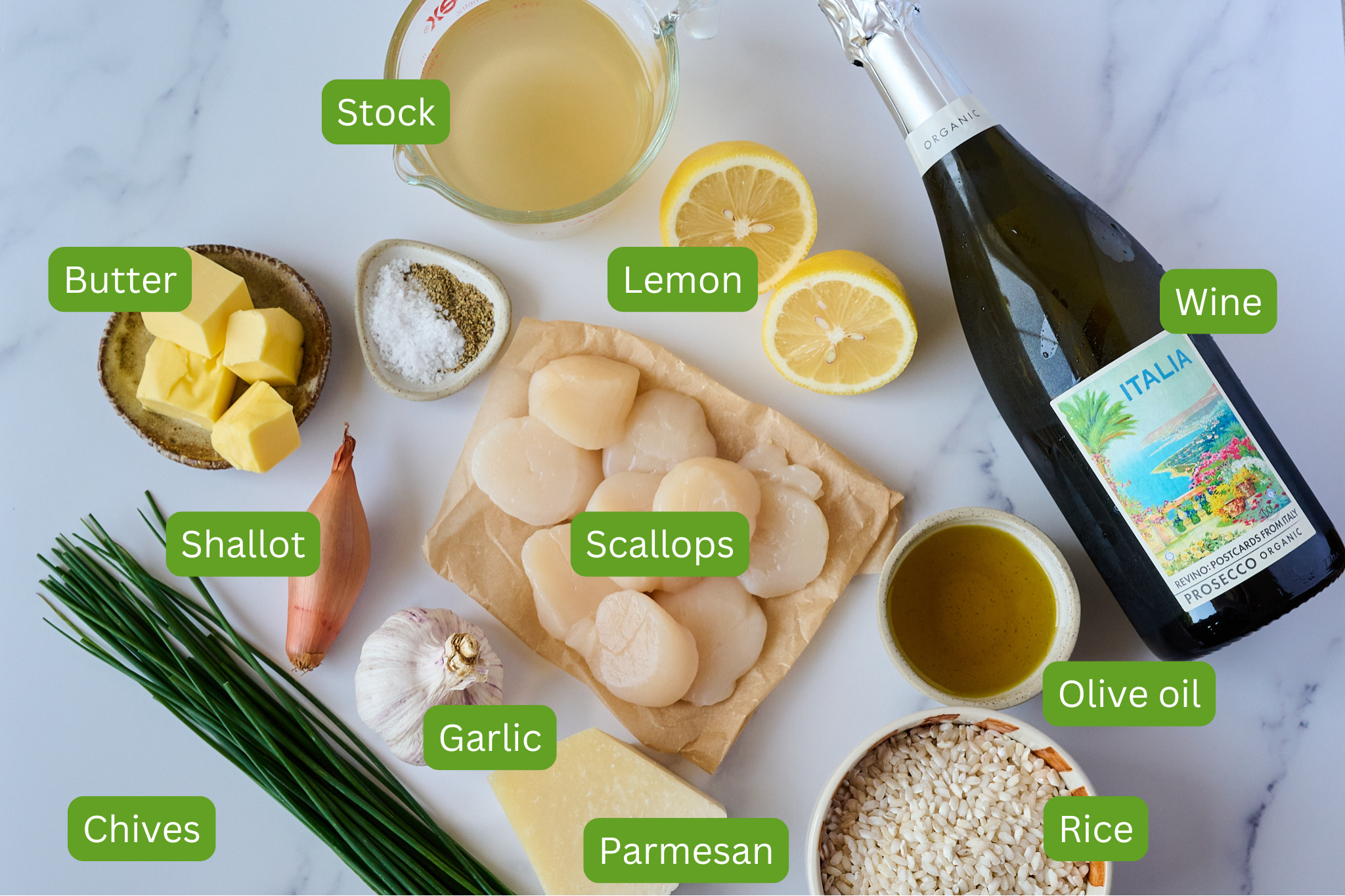 Ingredients shot for scallop risotto are laid out on marble backdrop including stock, lemons, butter, shallot, garlic, chives, parmesan, rice, olive oil and wine. 