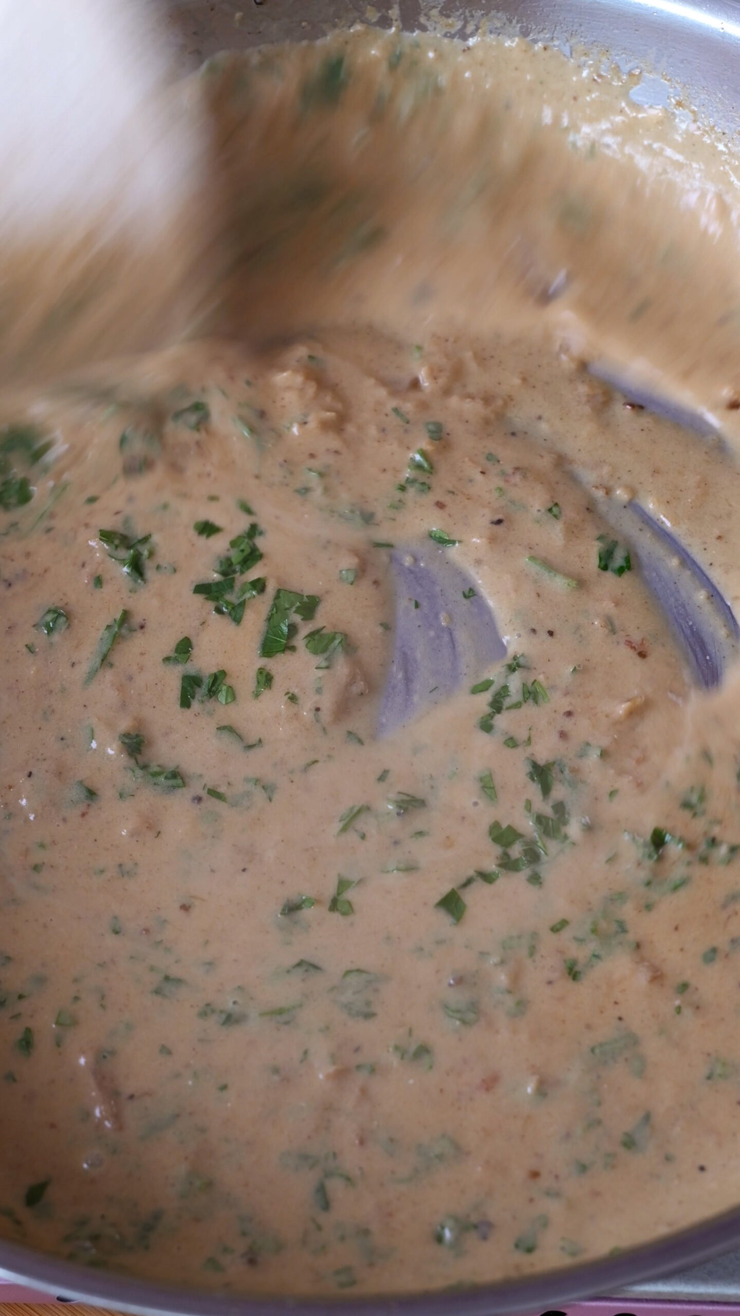 A creamy sauce is shown in stainless steel pan with fresh parsley sprinkled all over. 