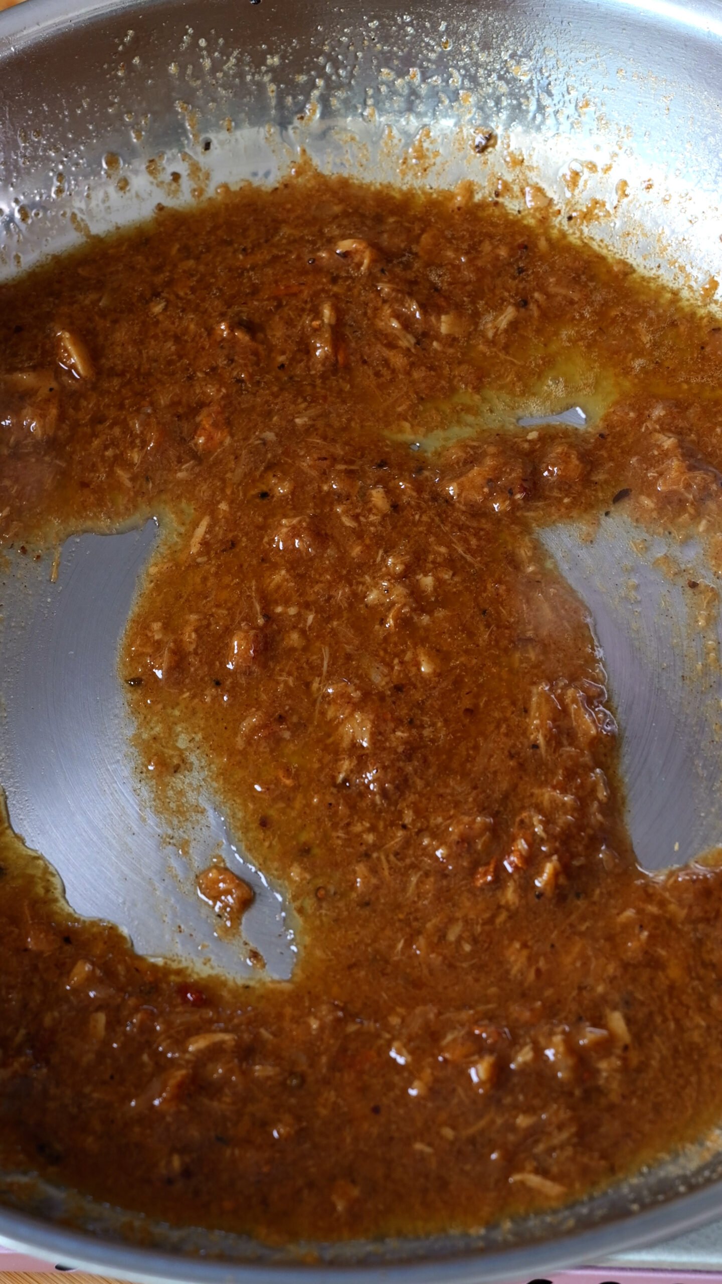 A brown sauce is shown in stainless steel pan. 