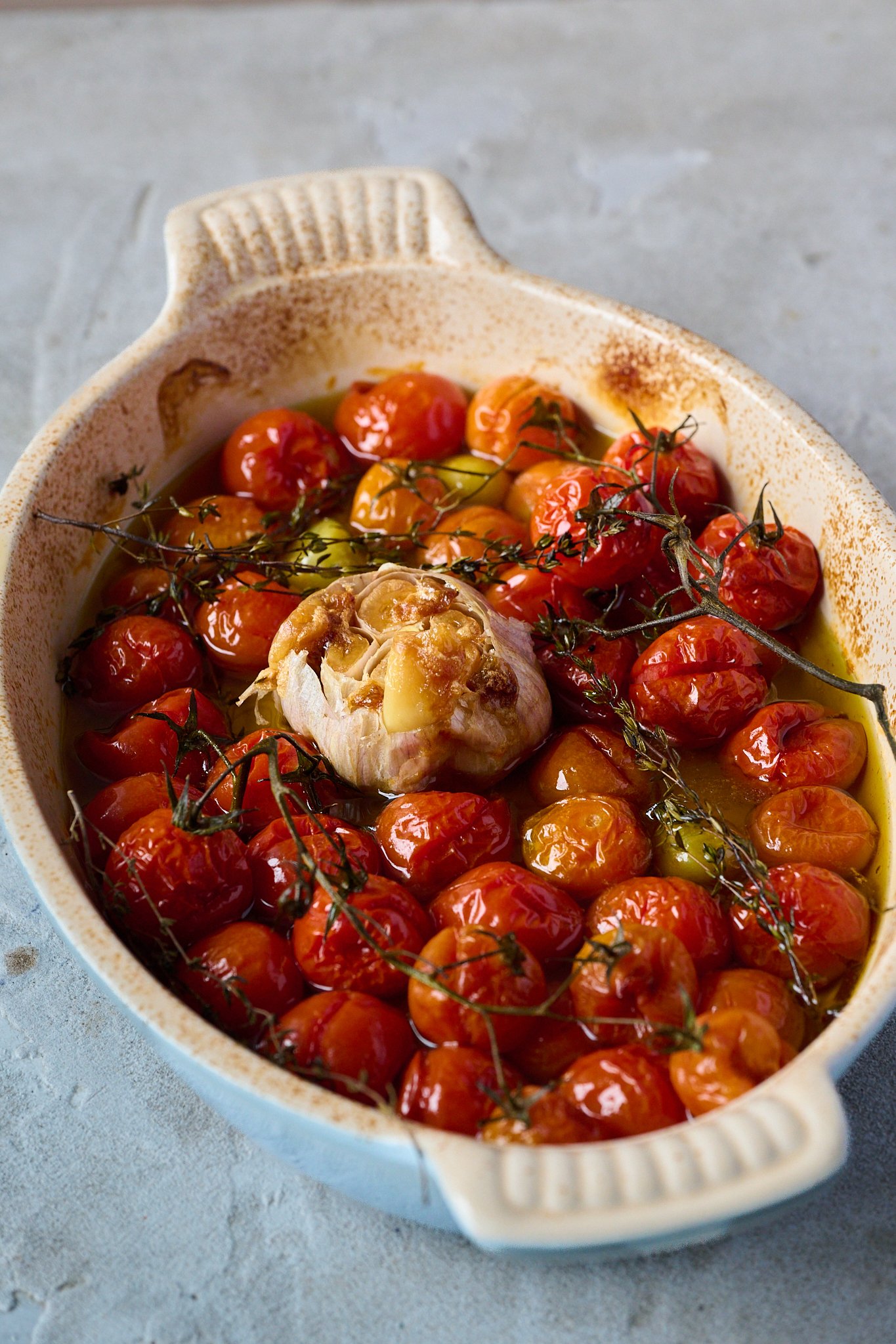 A large roasting dish is filled with baked cherry tomatoes and garlic. 