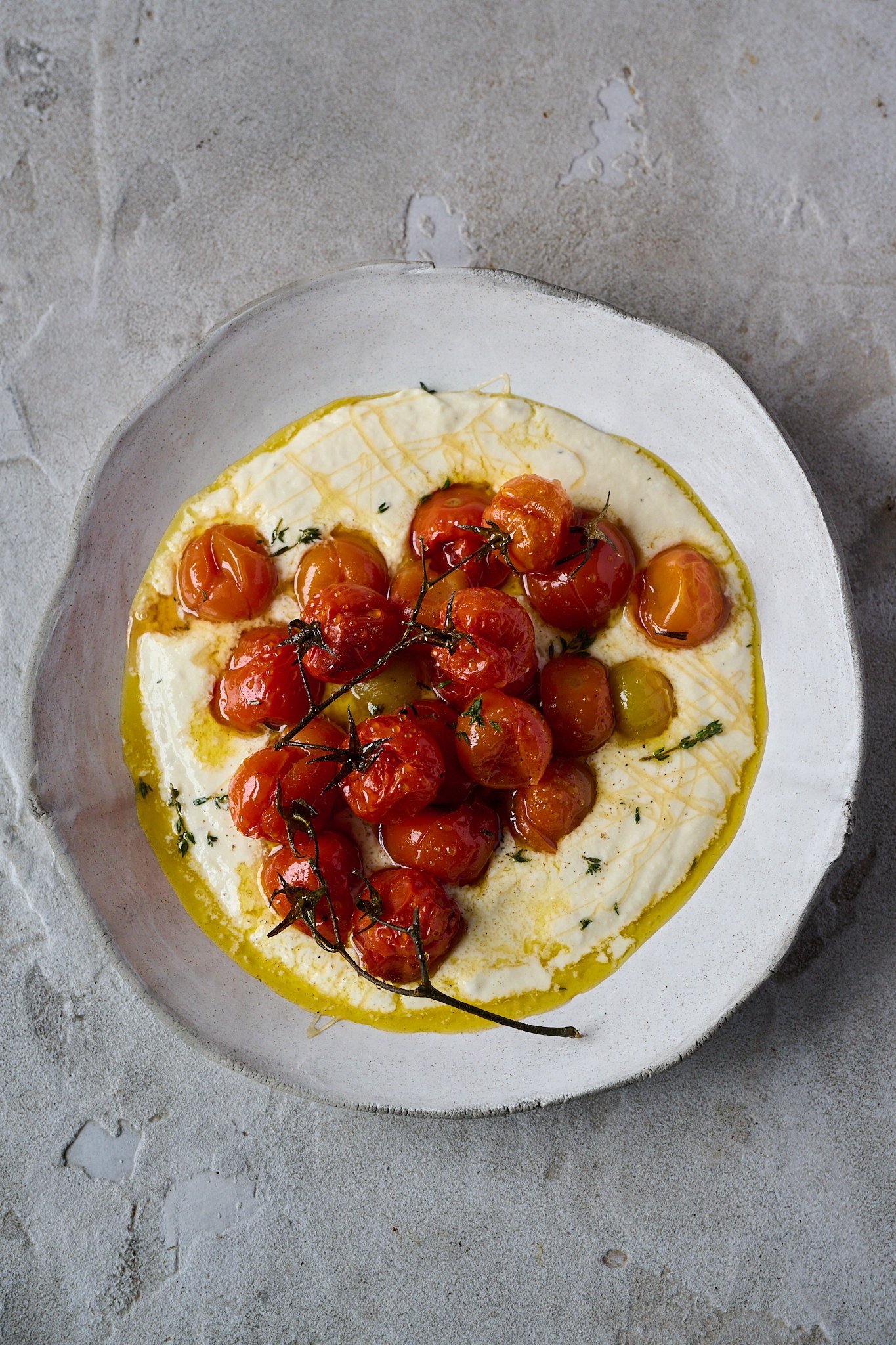 Large white plate is shown with whipped goat cheese and roasted tomatoes sitting on top. You can see a drizzle of honey and fresh thyme sprinkled all over.