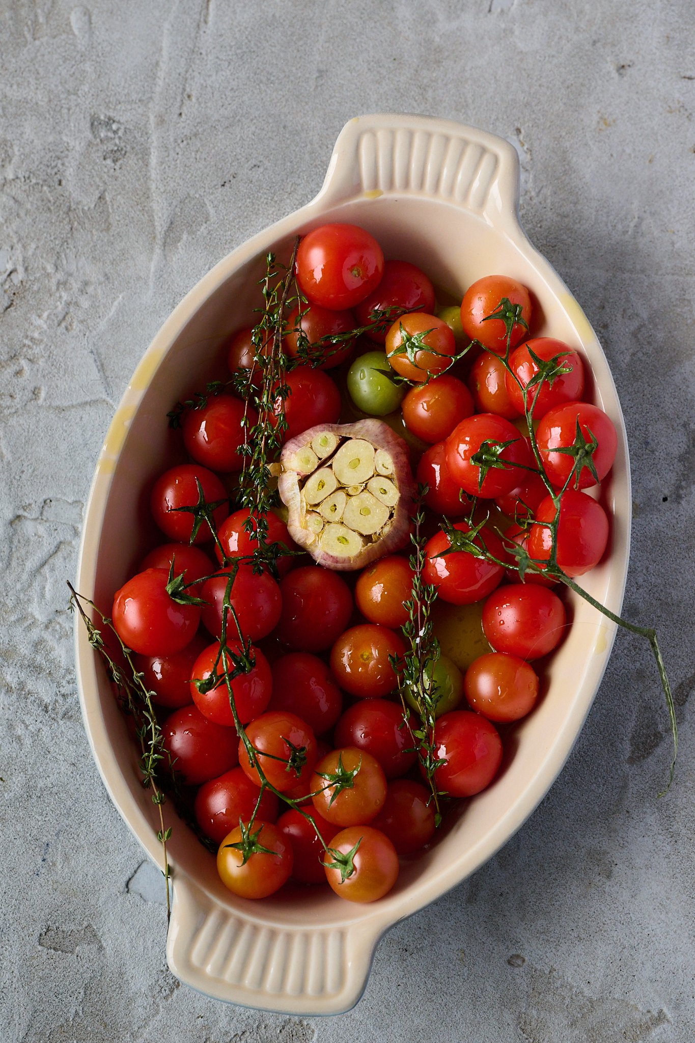A large roasting dish is filled with cherry tomatoes and garlic. 