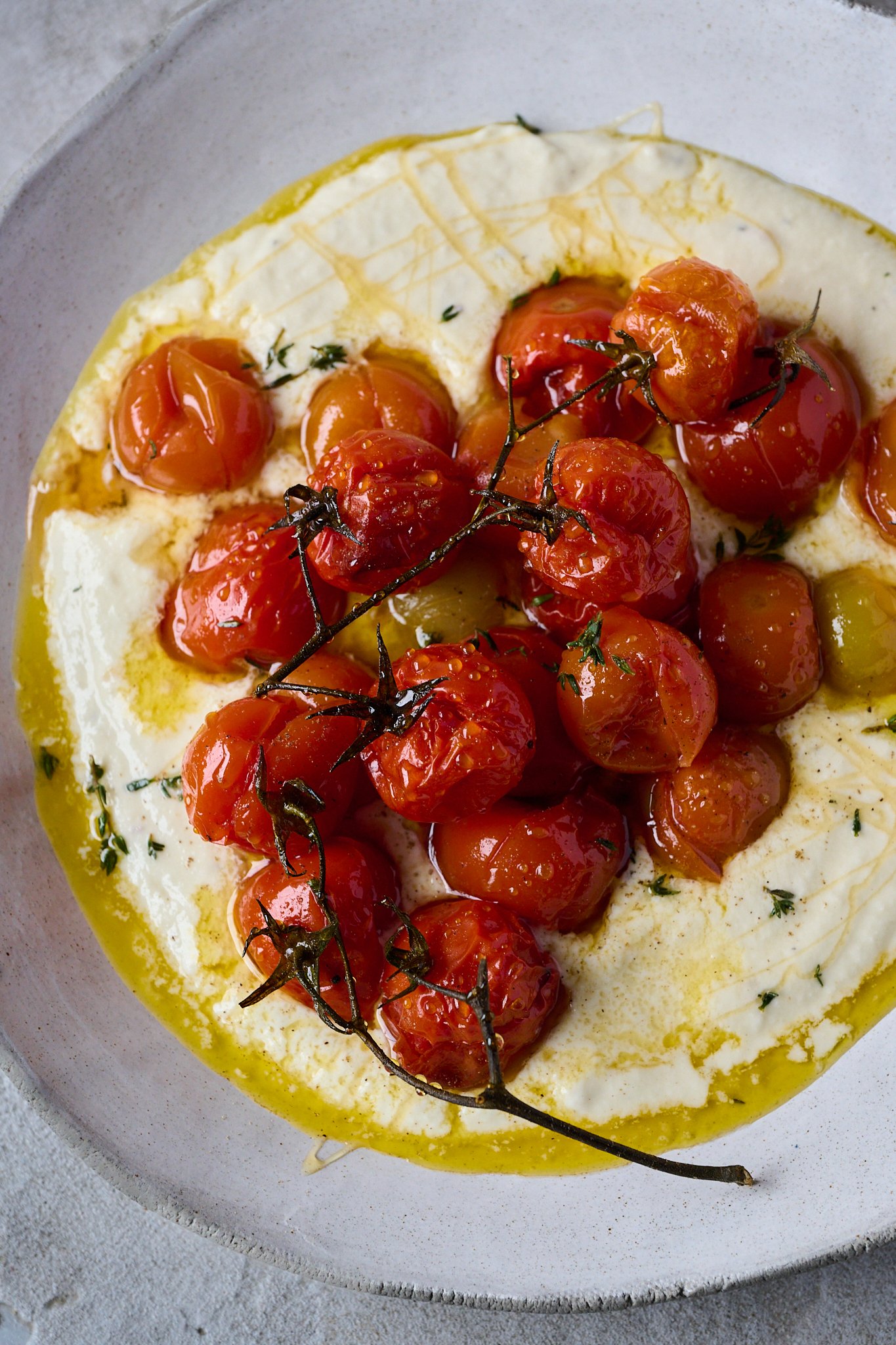 Large white plate is shown with whipped goat cheese and roasted tomatoes sitting on top. You can see a drizzle of honey and fresh thyme sprinkled all over. 