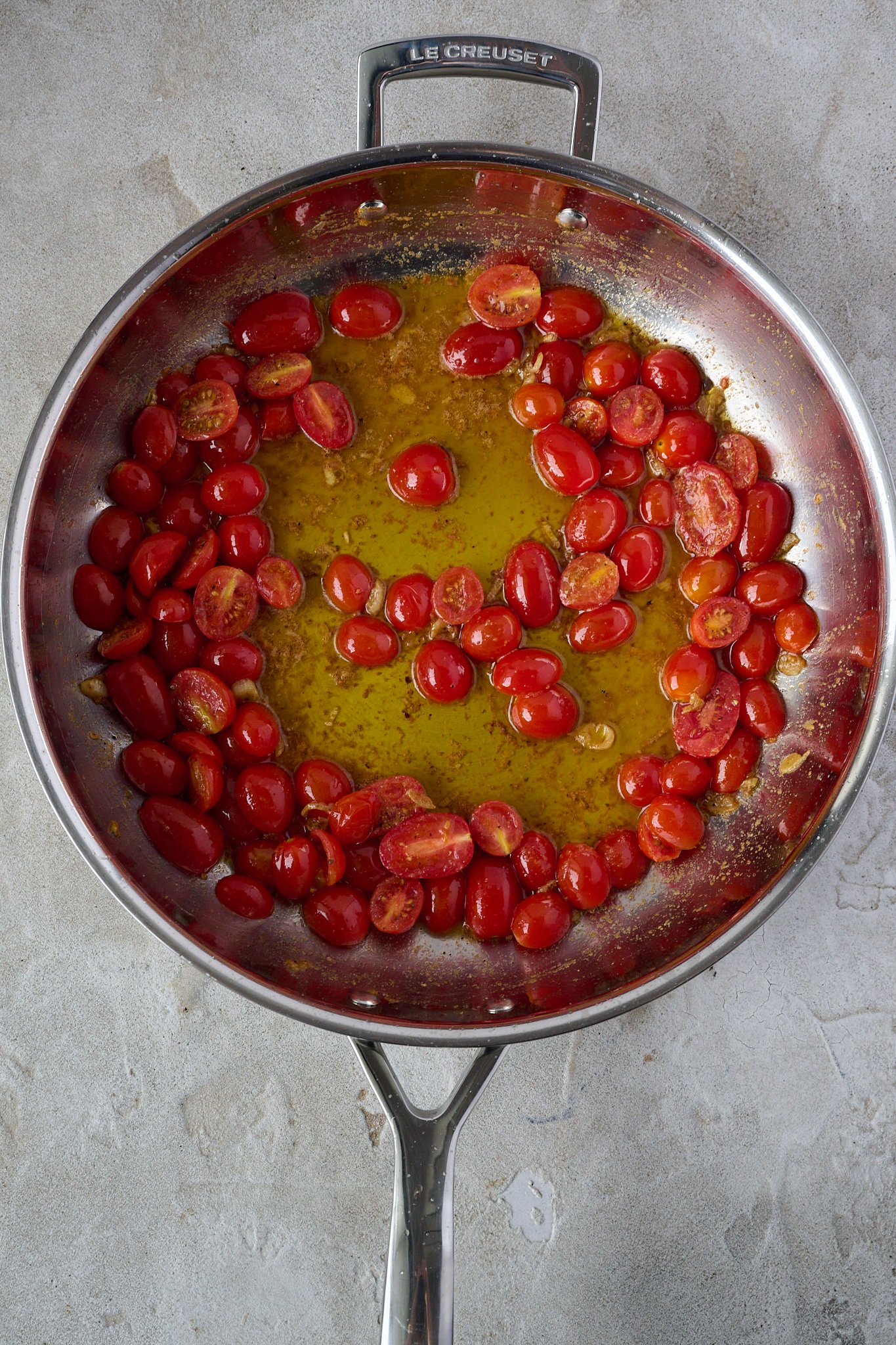 Large stainless steel pan is shown with cooked cherry tomatoes and melted butter. 