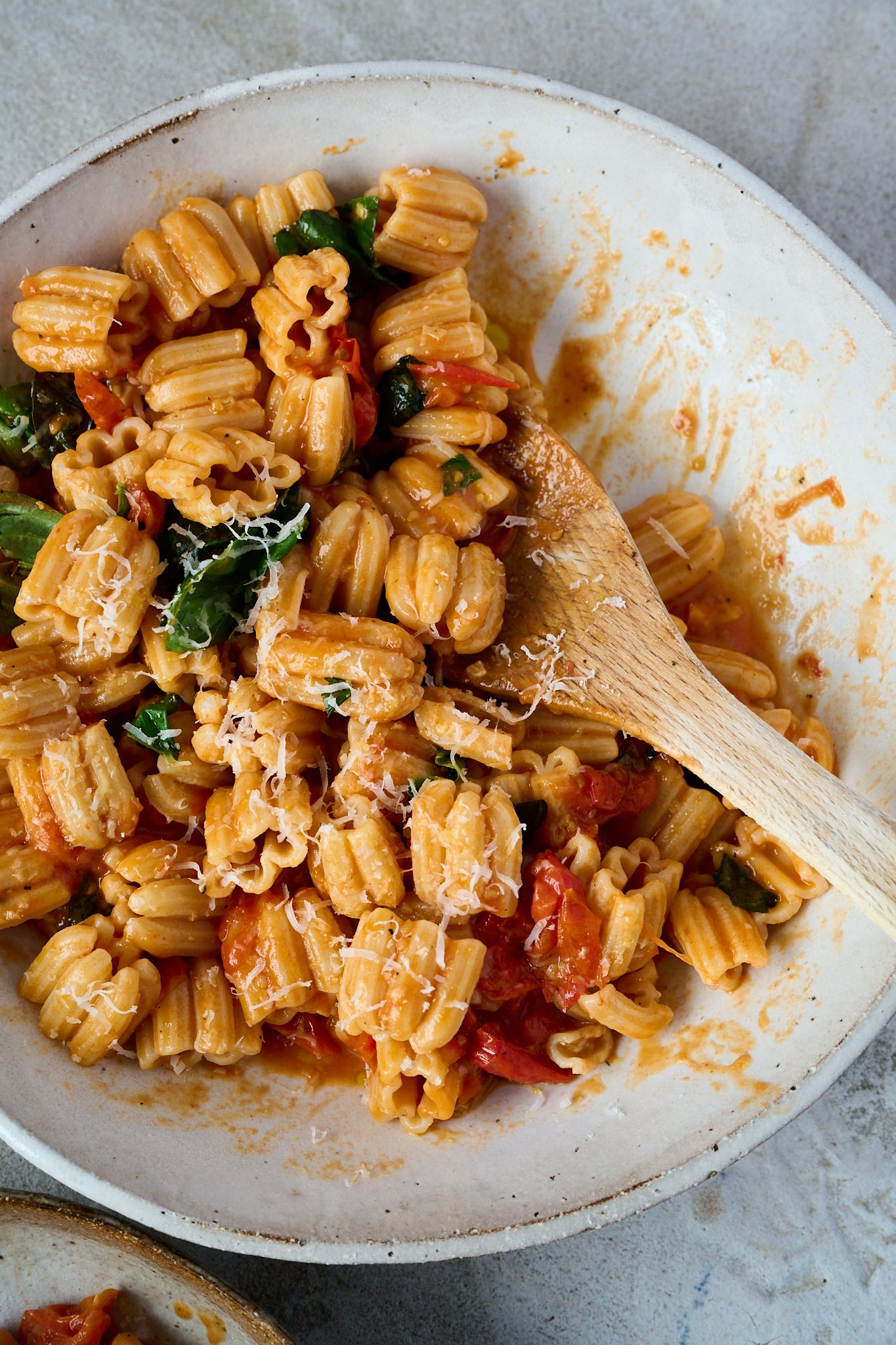 Tomato and butter pasta sits in large white bowl with fresh basil sprinkled all over and some grated parmesan cheese. Wood spoon is sticking out the right side of the bowl. 