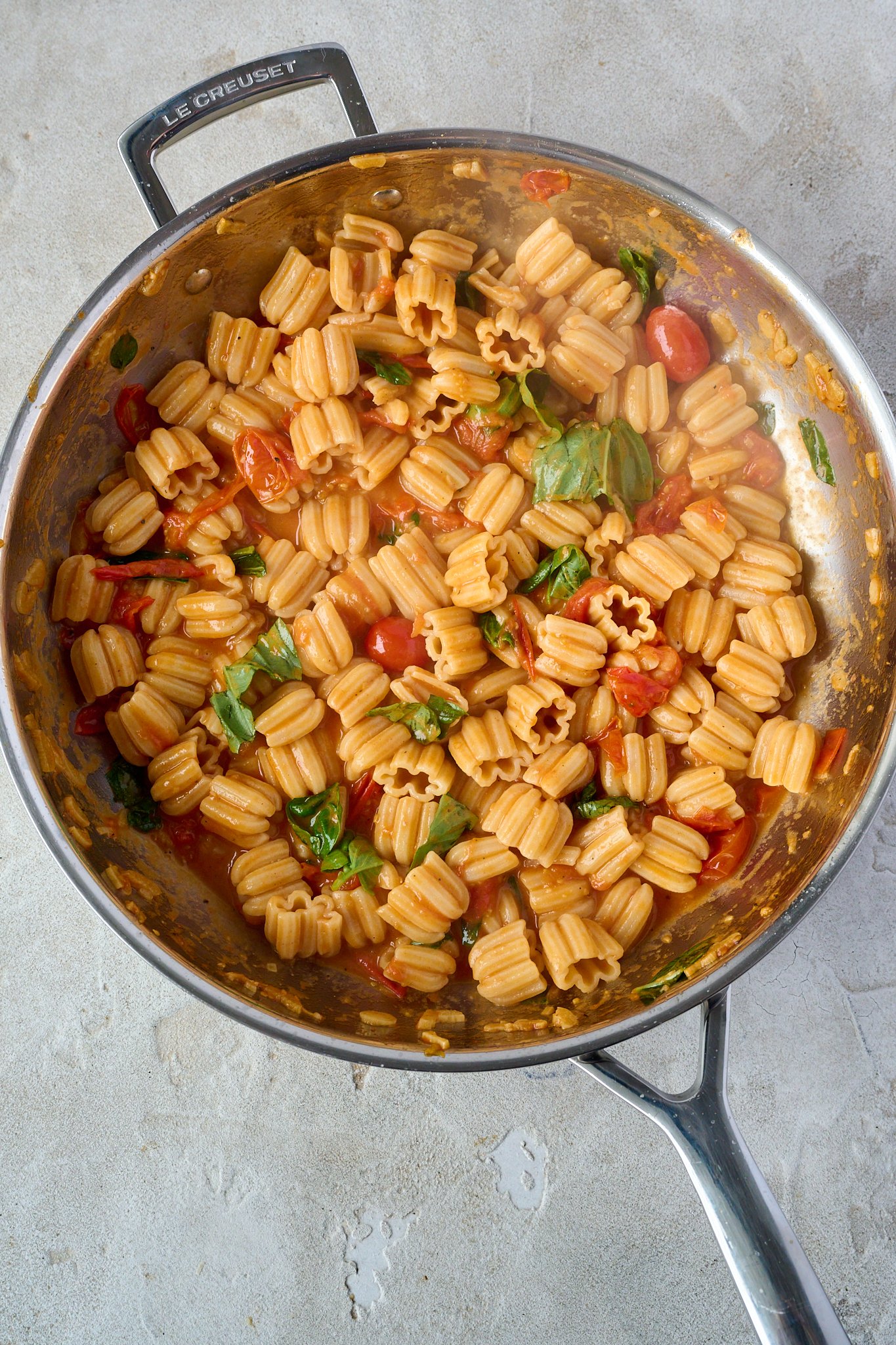 Tomato and butter pasta sits in large stainless steel pan with fresh basil sprinkled all over. 