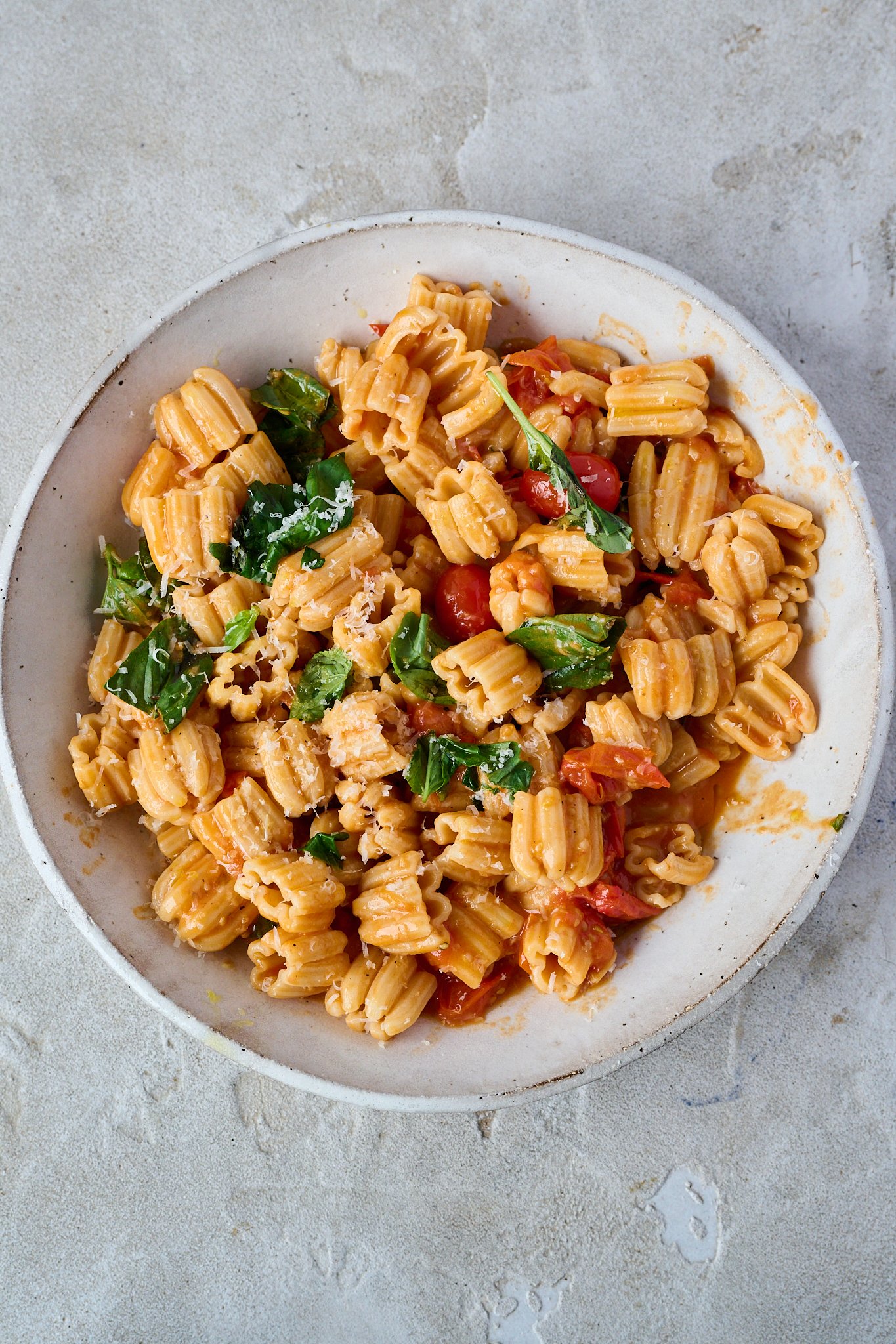 Tomato and butter pasta sits in large white bowl with fresh basil sprinkled all over and some grated parmesan cheese.