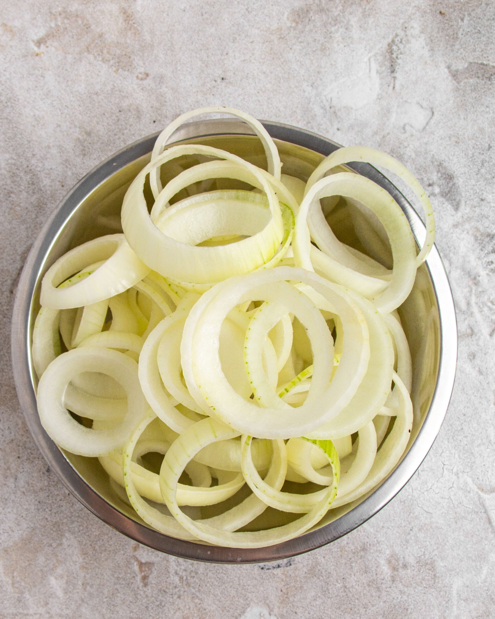 Onion rings sit in metal bowl. 