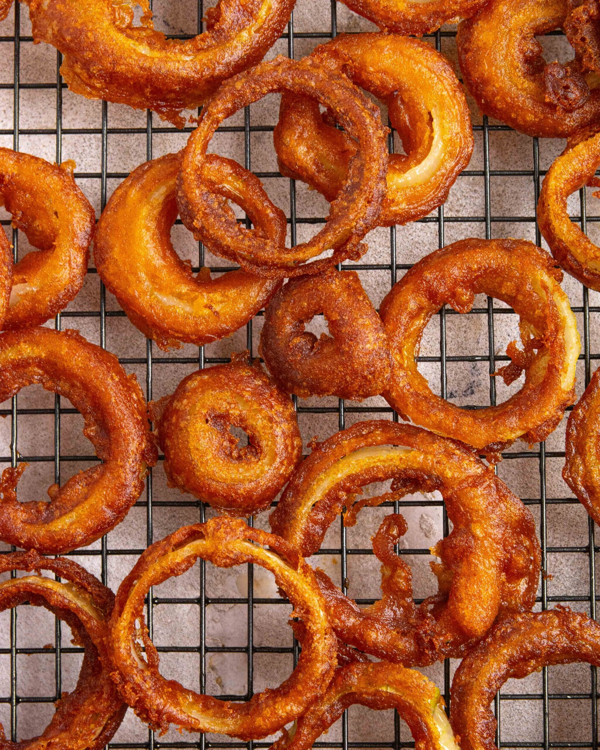 Beer battered onion rings are laying onto cooling rack