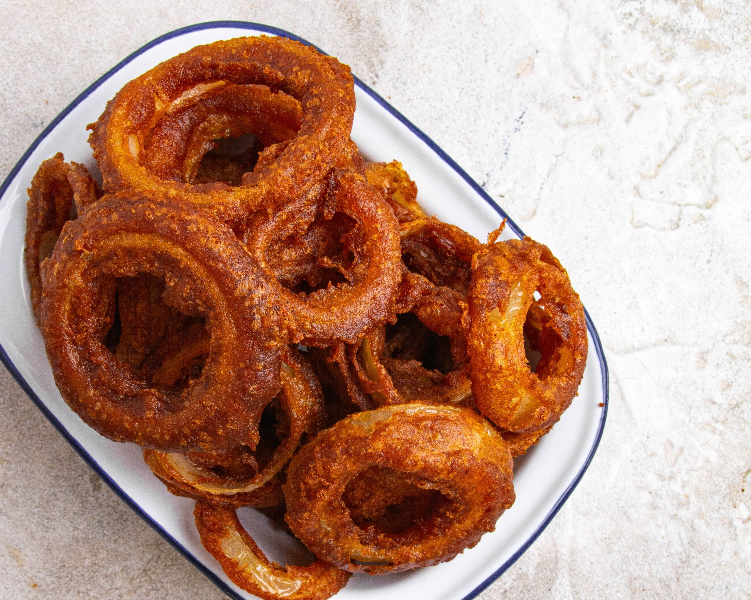 Beer battered onion rings sit in white tray with blue trim. 