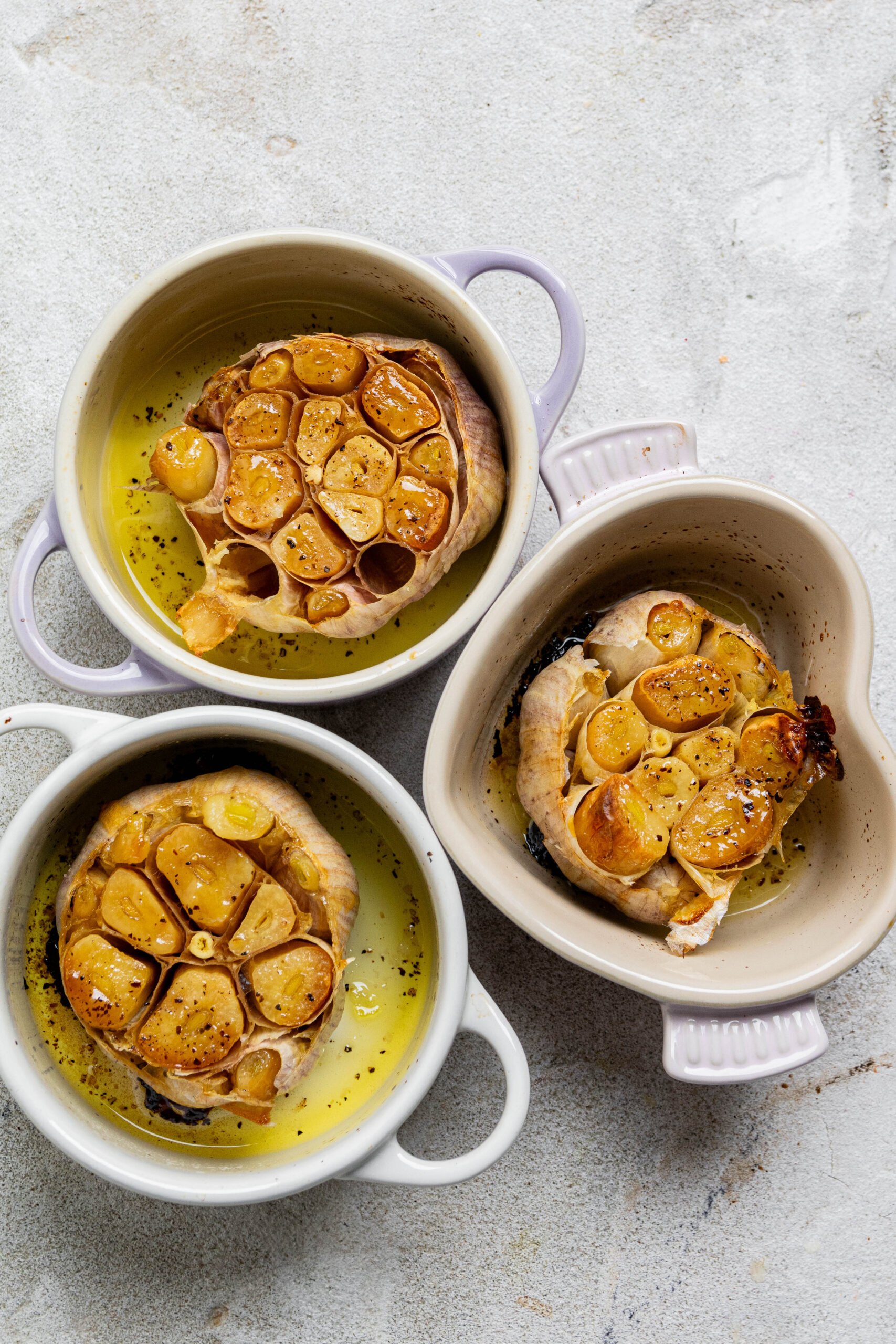 3 little pots are filled with roasted garlic bulbs. 