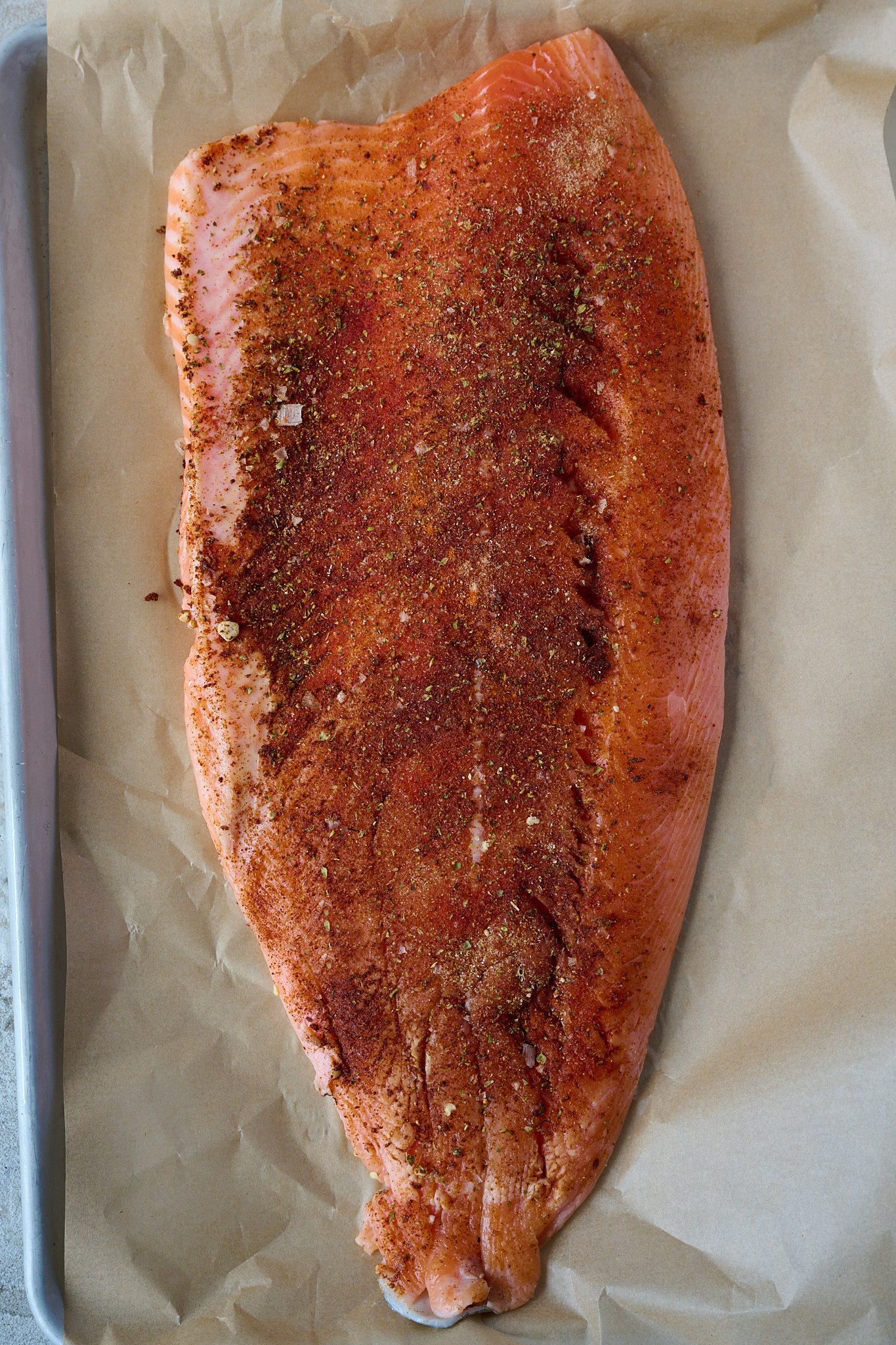 Raw salmon is on large baking tray and has been coated in spices