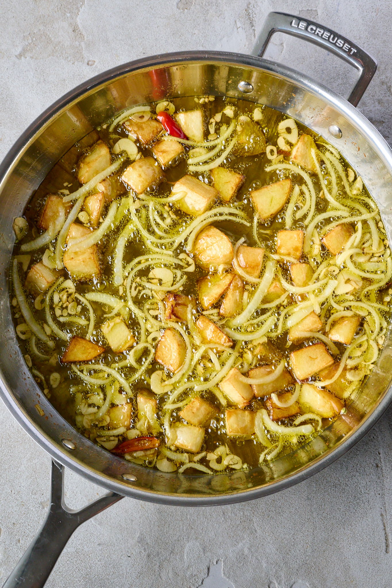 Potatoes, onion, garlic and chilli are fried in olive oil in large stainless steel pan.