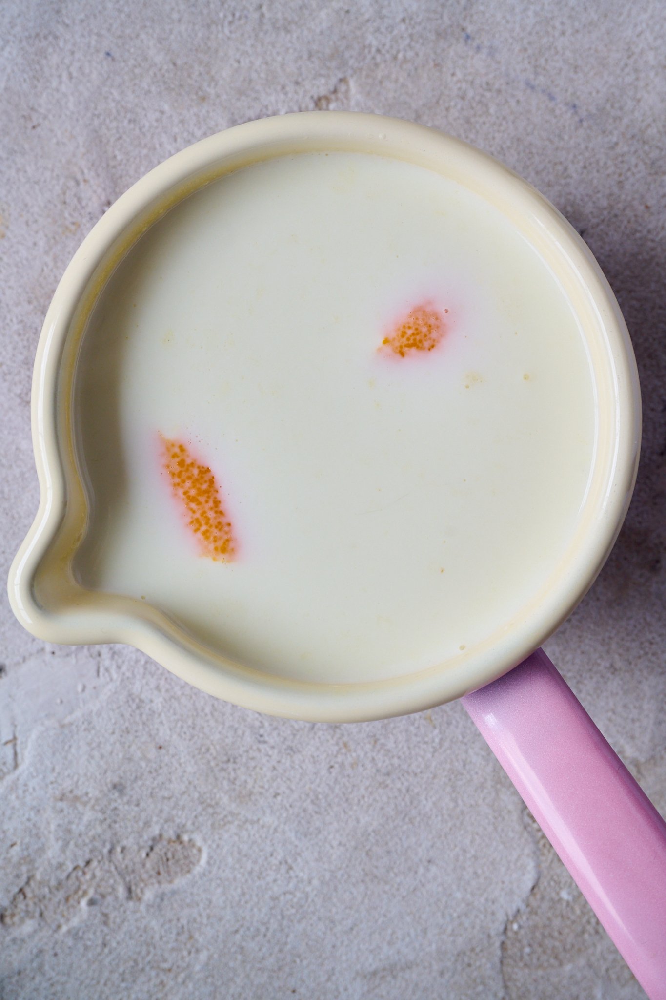 A small pink pot is filled with milk and slices of orange peel. 