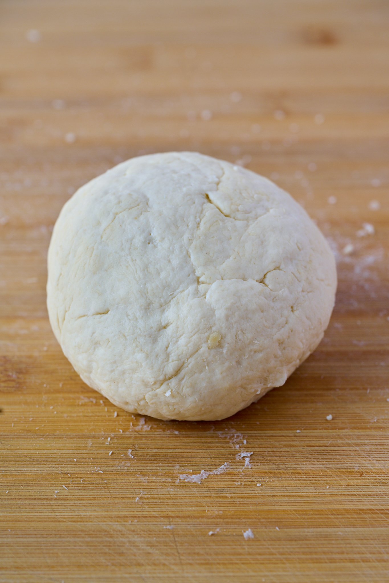 a ball of dough sits on a wooden chopping board