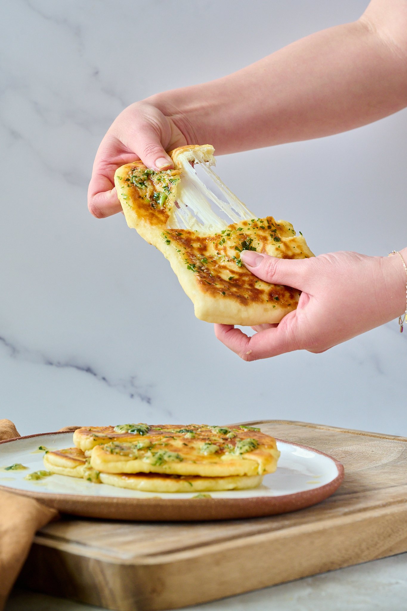 3 Ingredient yogurt flatbreads are piled on top of each other and sit on a white plate. They are drizzled with garlic butter. One flatbread is being pulled open and you can see the cheese pulling out.