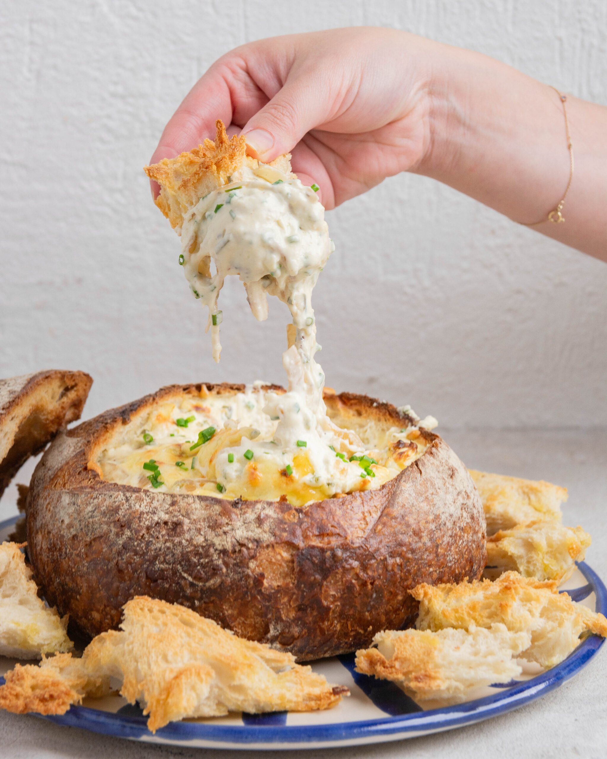 French onion dip cob loaf is being dipped into with a large piece of bread. You can see the dip coming out of the cob loaf. 