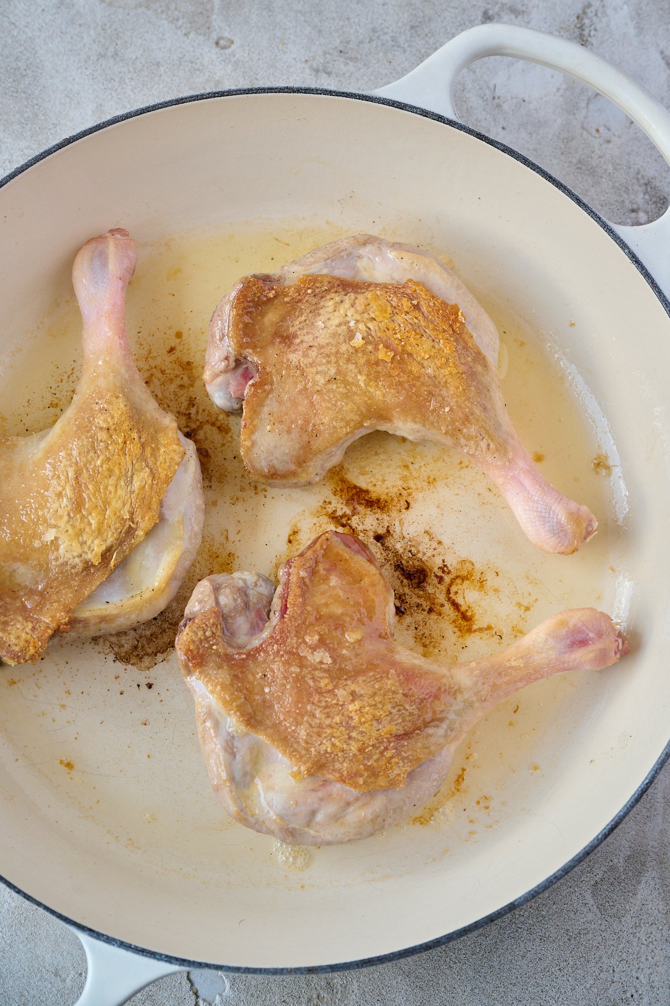Three duck legs are in a white pan and have crispy skin.