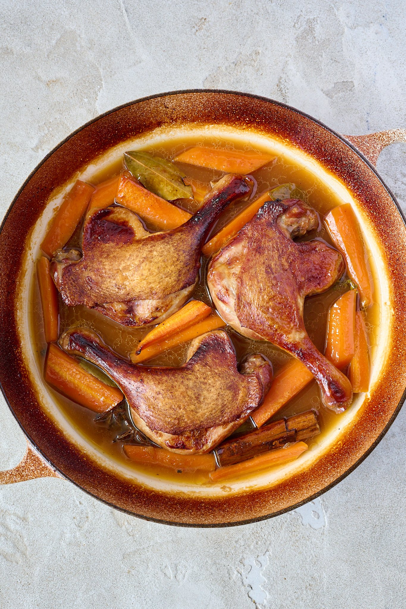 Crispy duck legs are shown in a white pan with brown sauce and carrots.