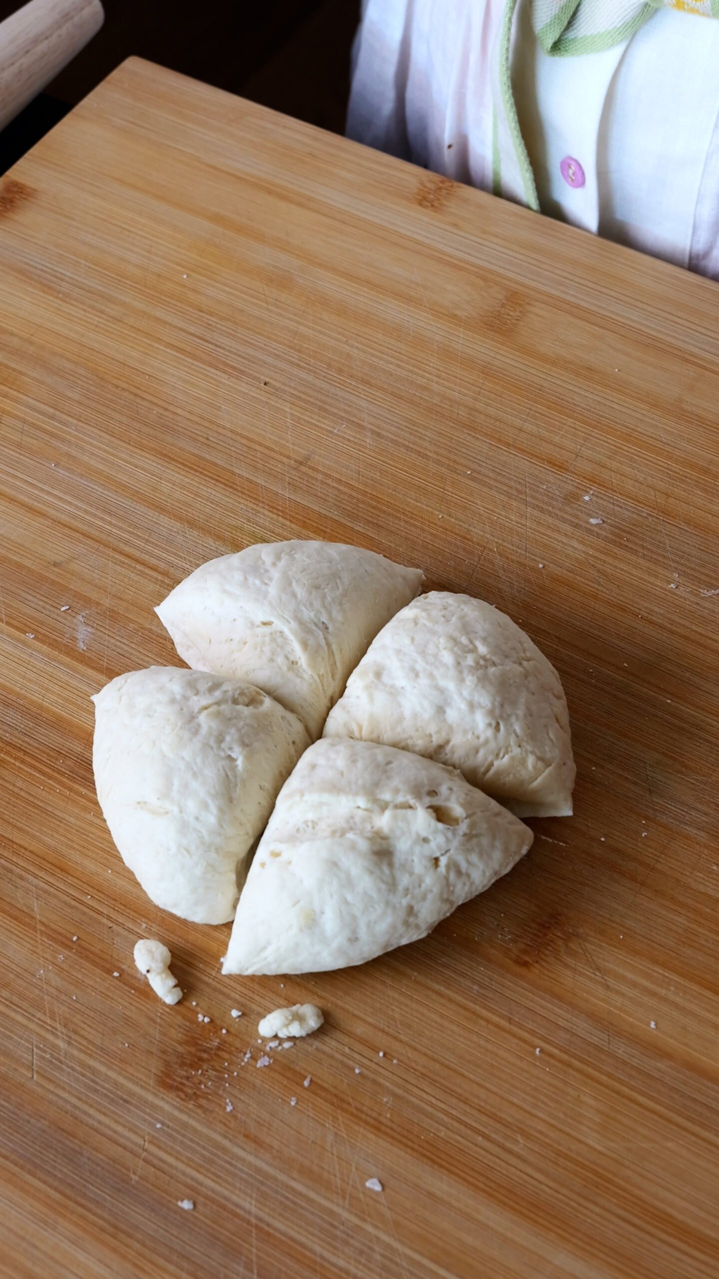 Dough is on wooden chopping board and divided into four.
