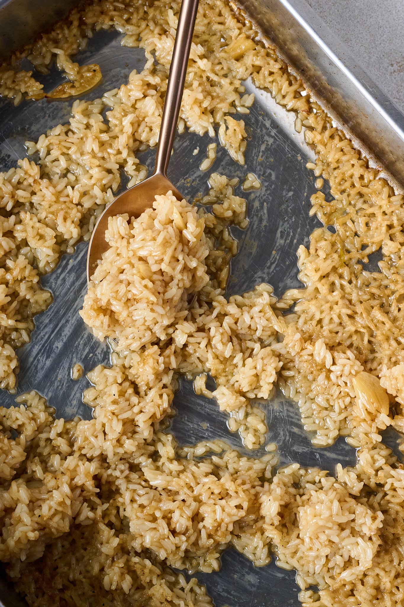 Cooked rice is in baking tray with golden spoon